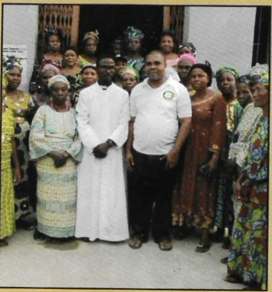 Group photo — KUTH team with a priest and widows at the home entrance