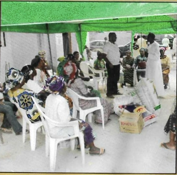 Widows seated under the green canopy with cartons of provisions