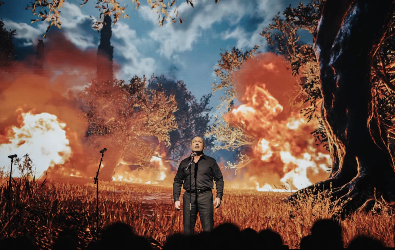 A vocalist performing before a dramatic fire projection