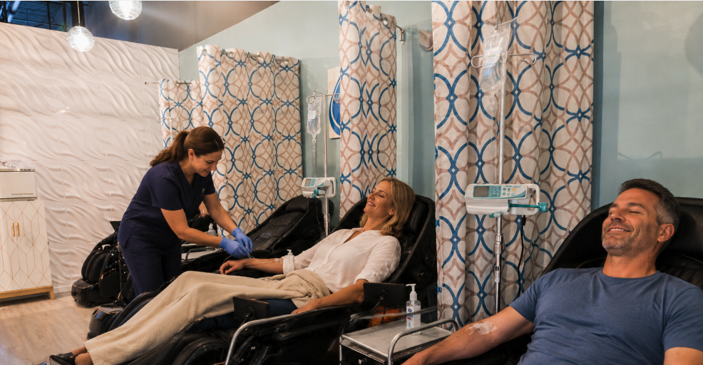 A Prime IV nurse tending to a smiling female client while a relaxed male client receives an IV drip in the Flemington lounge