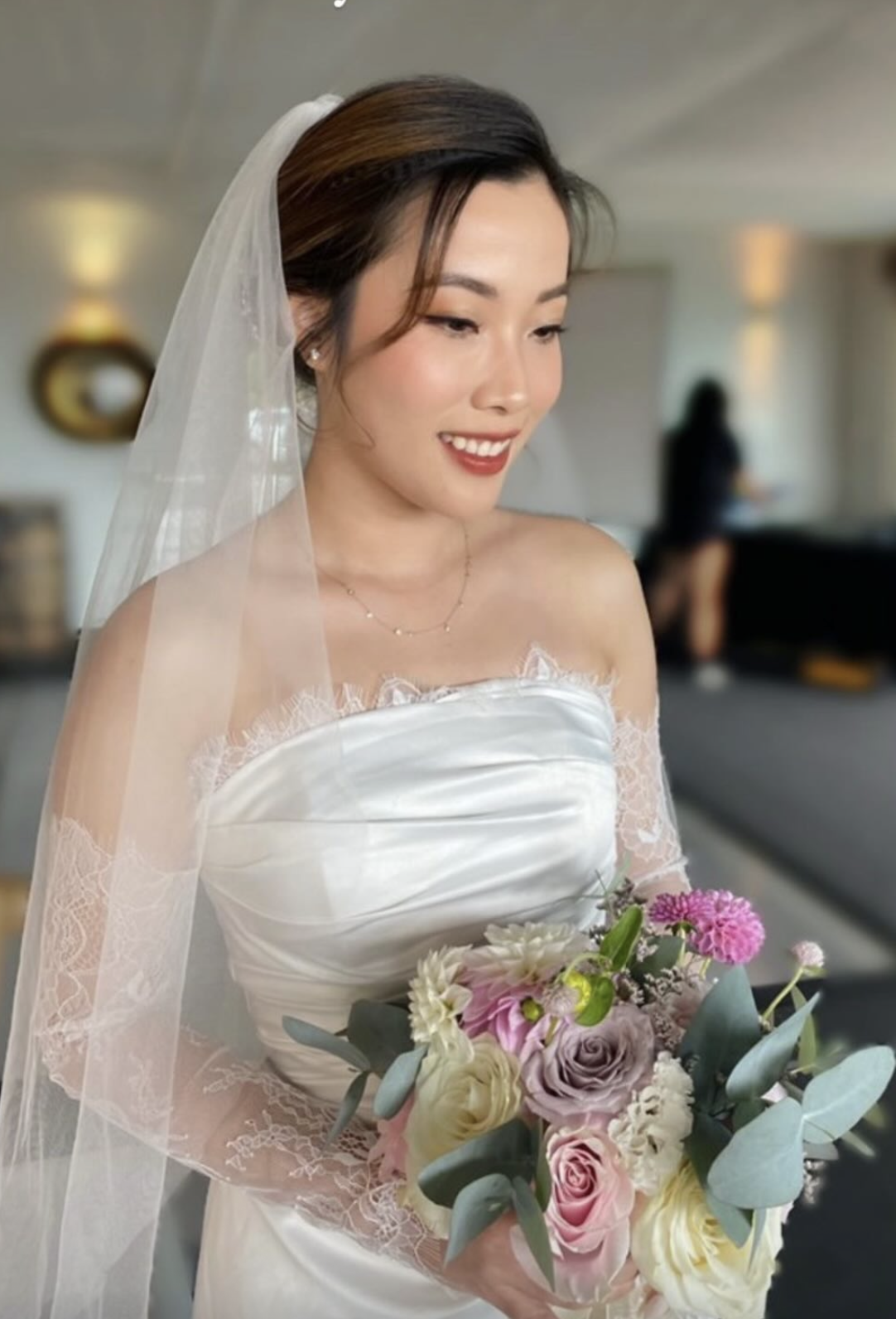 Bride in a veil and strapless satin gown holding a pastel bouquet with soft glam and a red lip