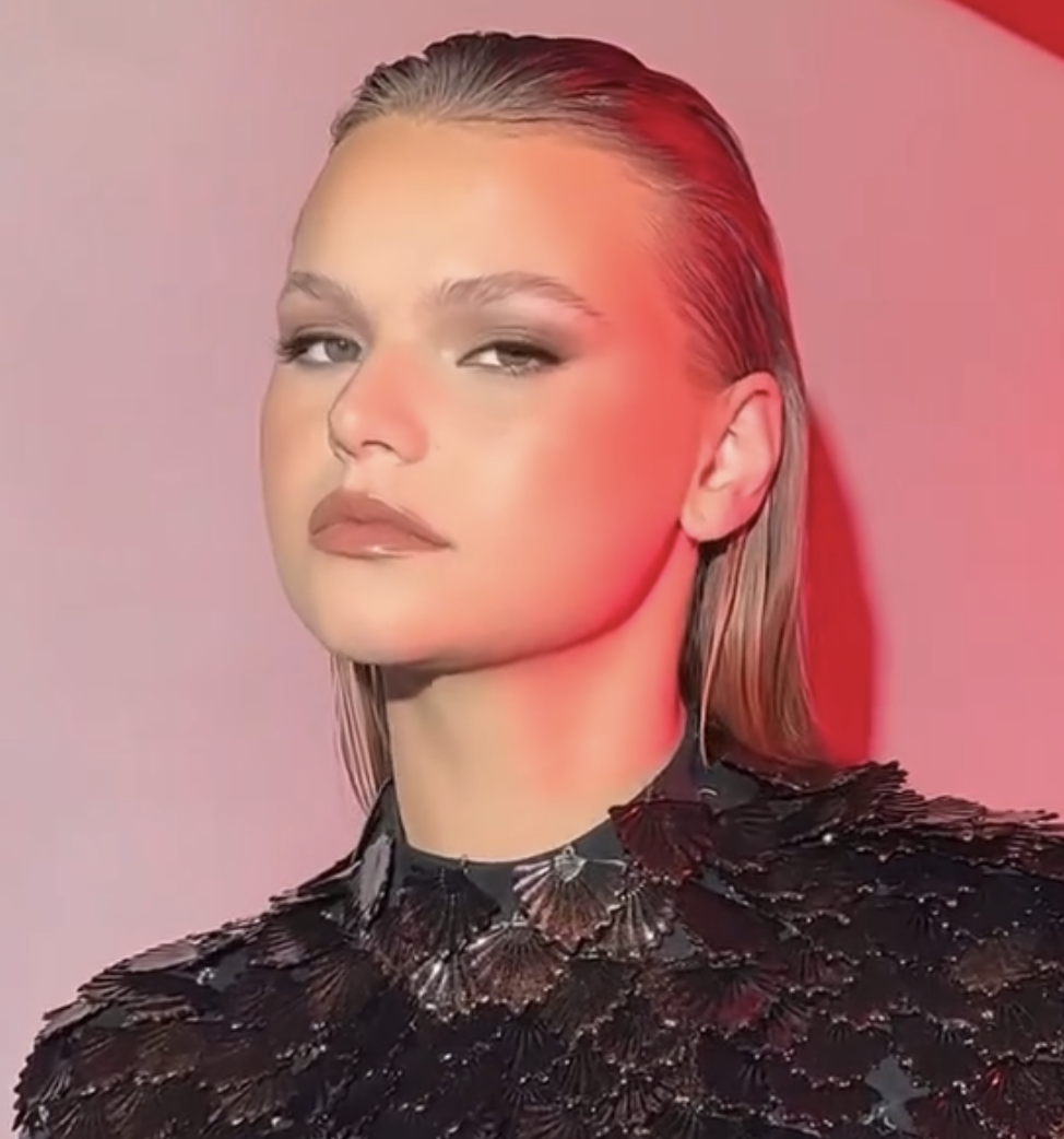 Editorial beauty shot of a model with slicked-back hair and smokey eyes under pink lighting