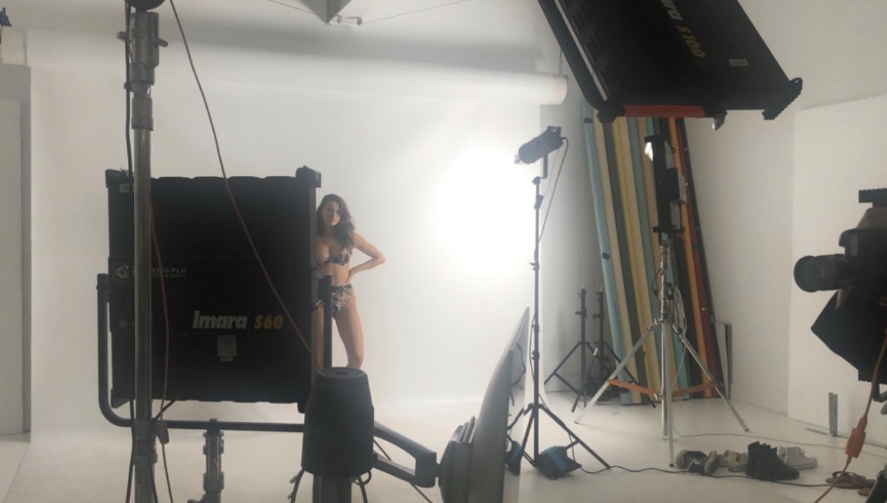 Behind the scenes of a studio photoshoot with a model on a white cyclorama and professional lighting