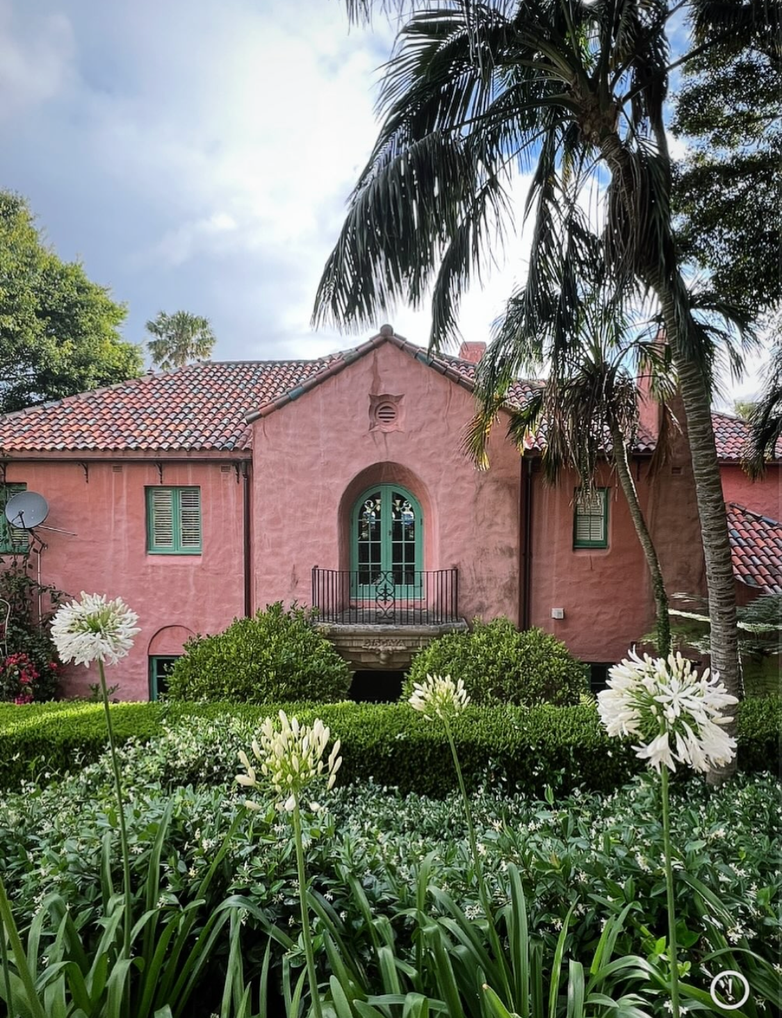 Villa Biscaya rear garden facade with arched green french door balcony, terracotta tile roof, white agapanthus flowers in the foreground and palm tree