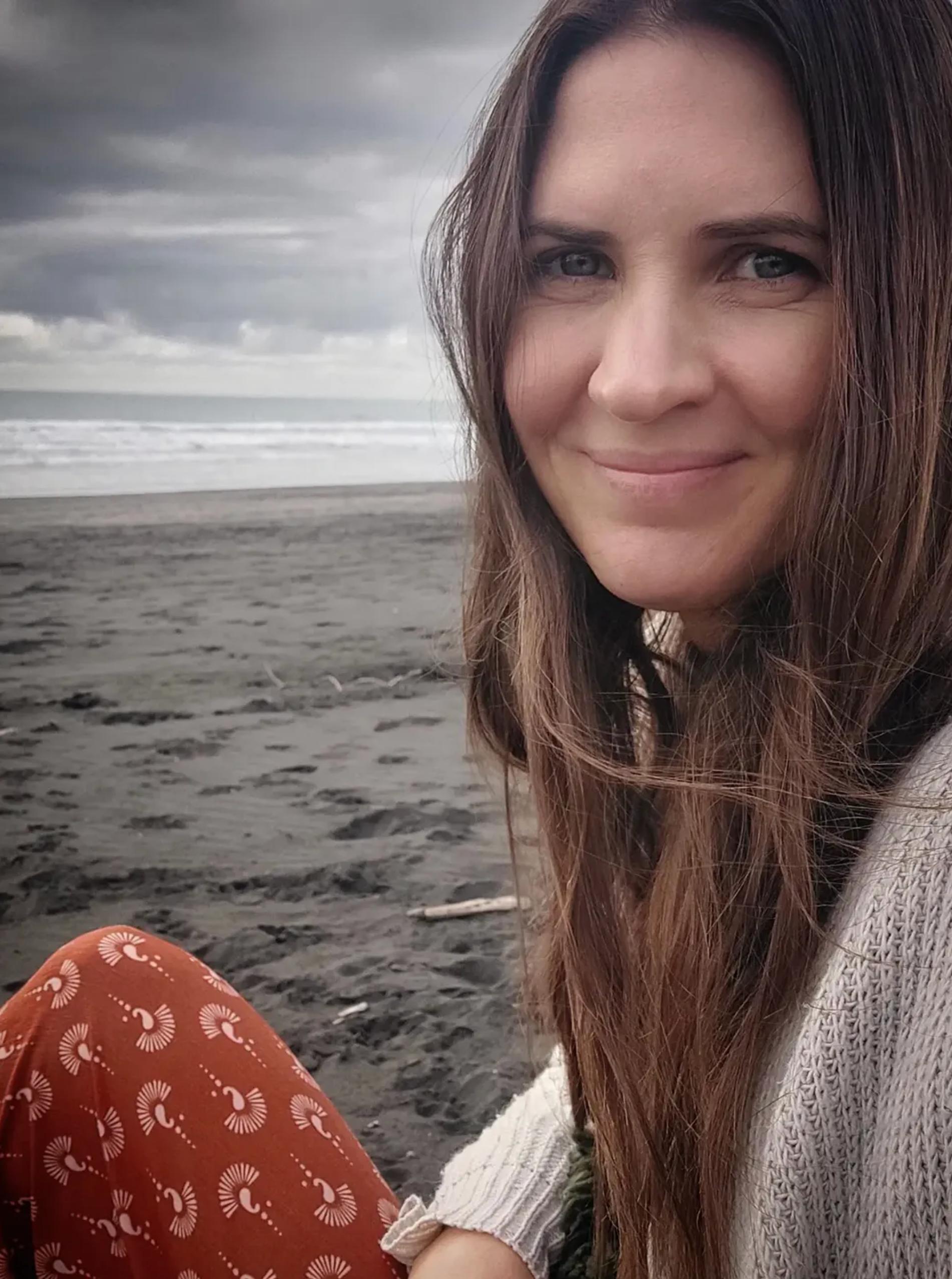 Julie Faulkner sitting on a dark sand beach, smiling warmly