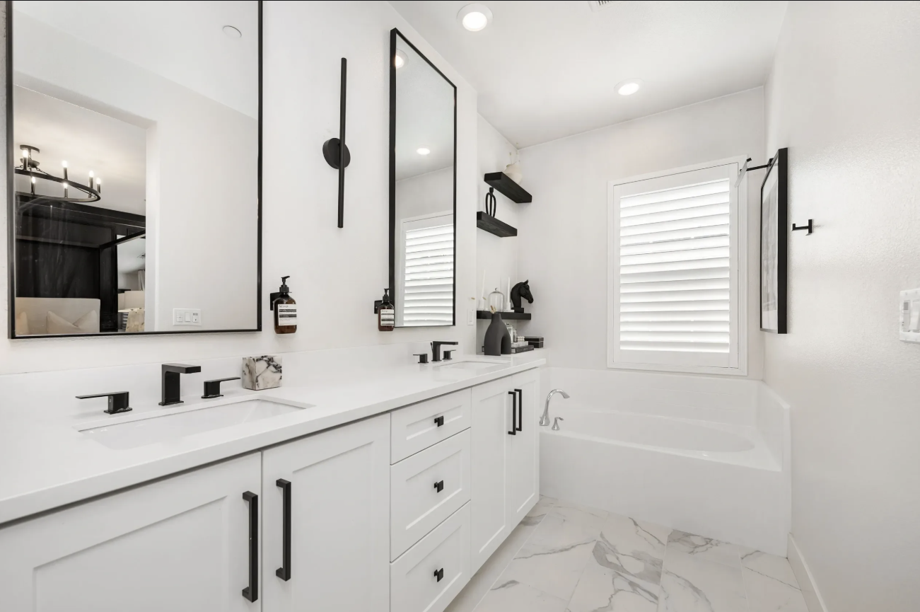 Modern white bathroom with double vanity, black frame mirrors, matte black fixtures, built-in soaking tub, and Calacatta marble floors