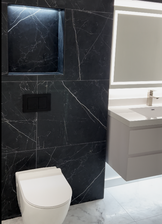 Black marble feature wall with illuminated niche, wall-hung toilet, gray floating vanity and backlit mirror