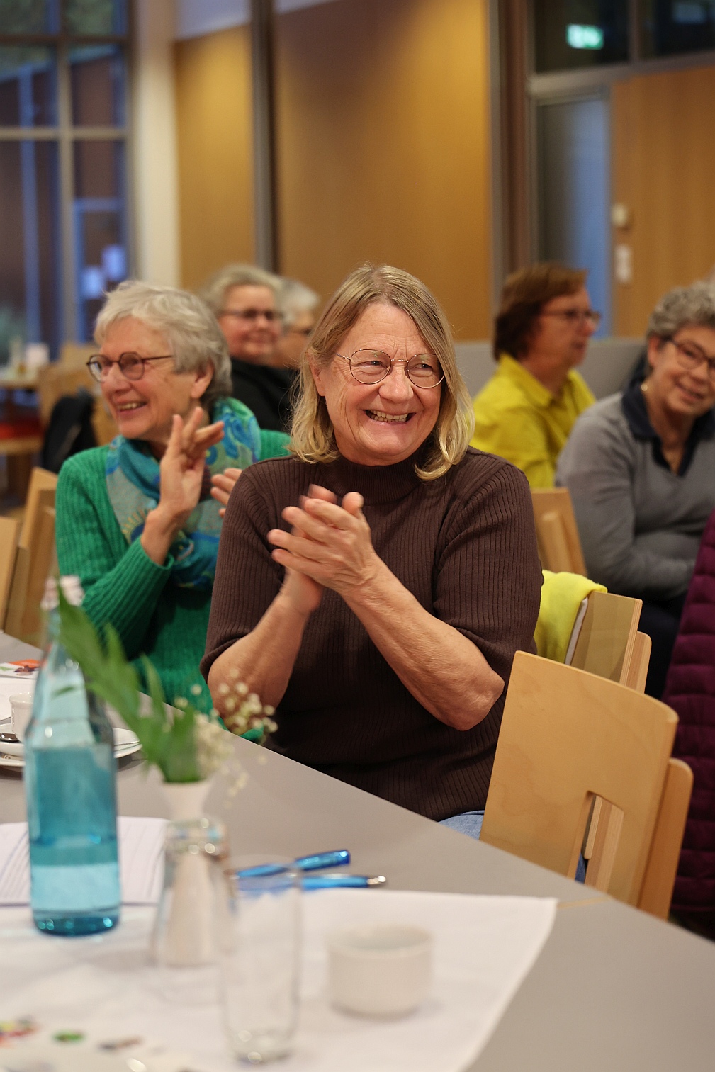Seniorinnen sitzen an Tischen in einem hellen Saal und applaudieren – Gemeinschaftsveranstaltung im Stadtteil