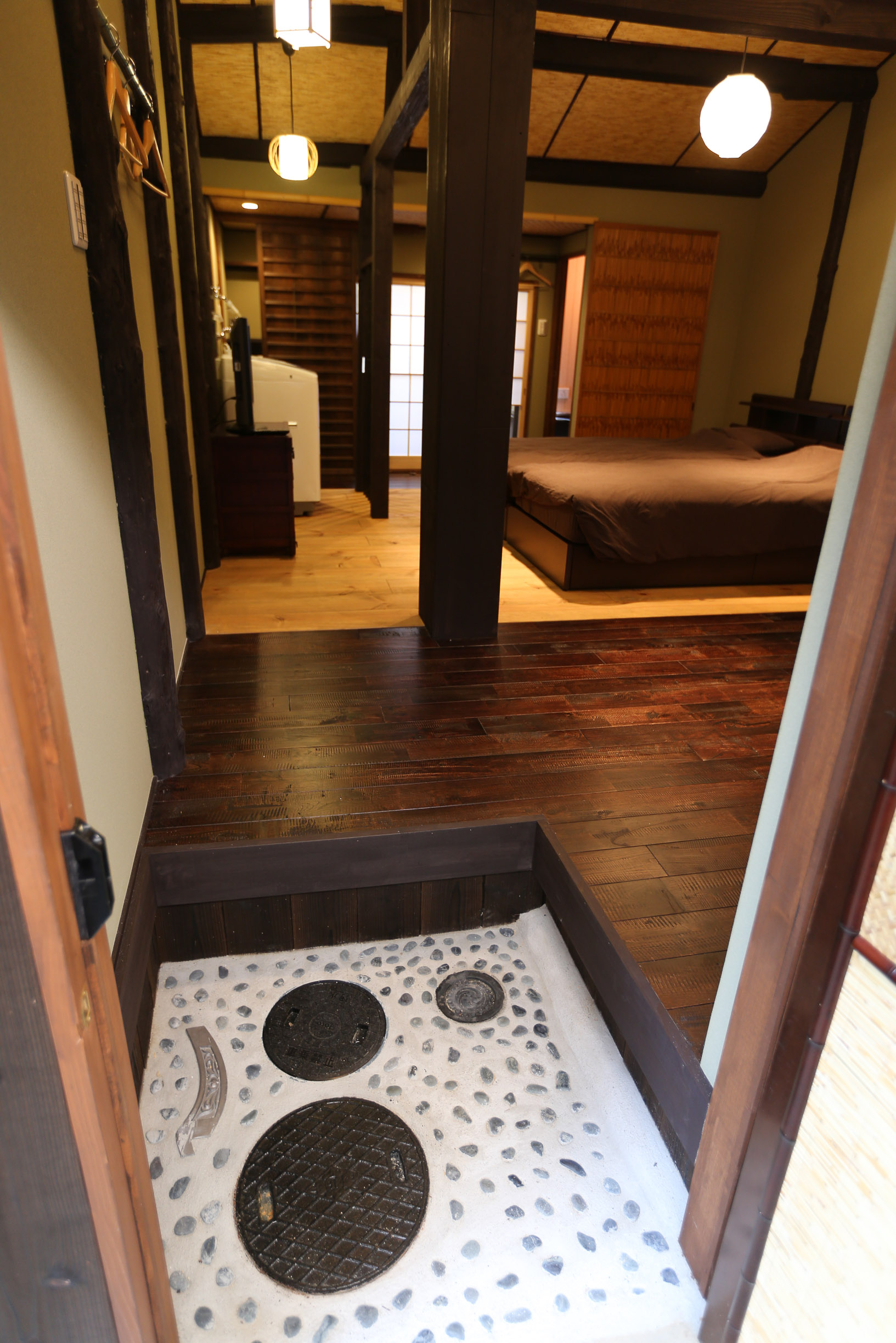 Traditional genkan entrance with river stone floor, dark wood steps, paper lanterns, woven bamboo ceiling, and view through to bedroom