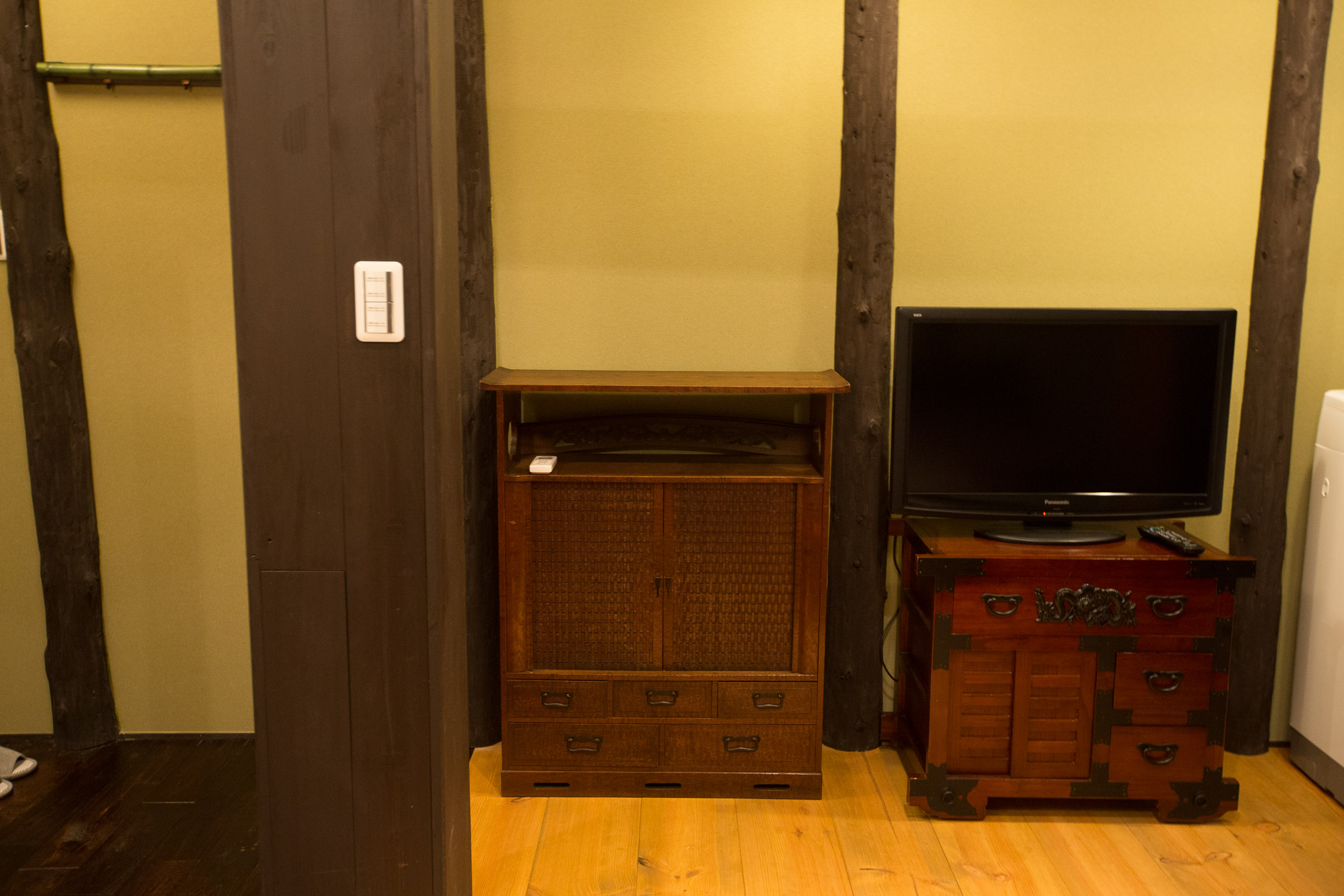 Living area with antique tansu cabinets, wicker-front chest, red lacquered chest with TV, dark wooden beams and ochre walls