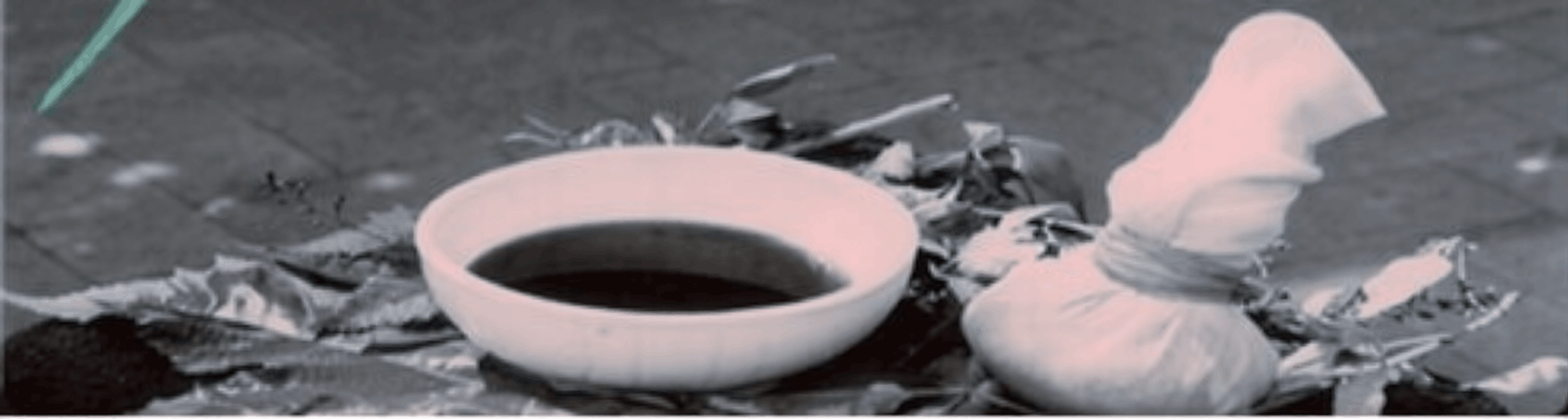 A ceramic bowl of dark herbal oil with fresh leaves and a wrapped herbal poultice