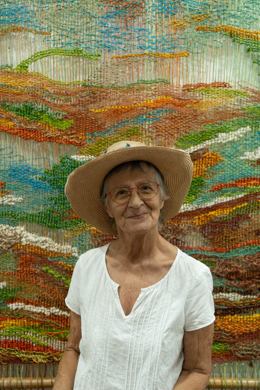 Silvia Medina sonriendo frente a uno de sus tapices tejidos