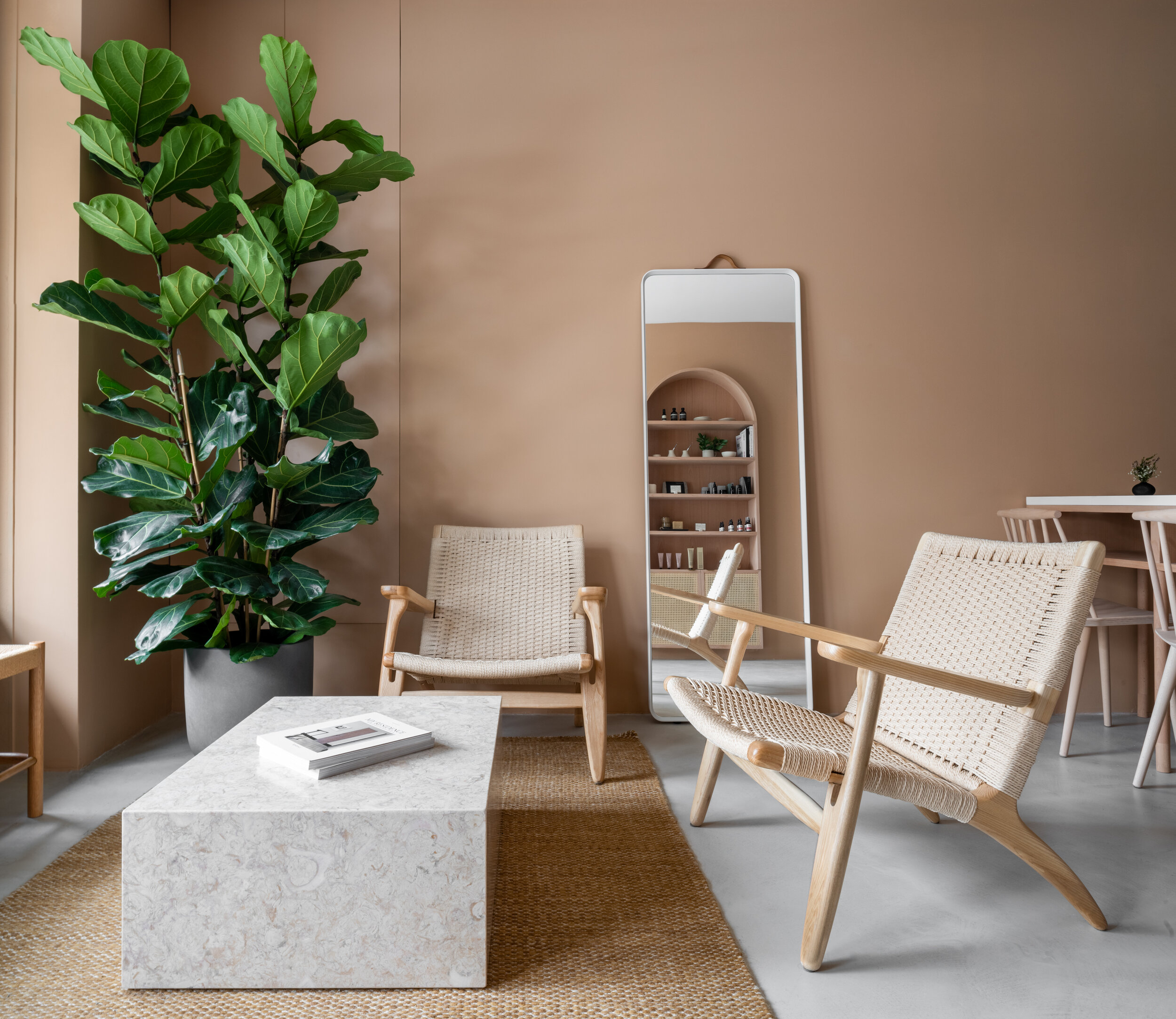 Minimalist waiting area with woven lounge chairs, marble coffee table, and fiddle leaf fig plant against warm beige walls