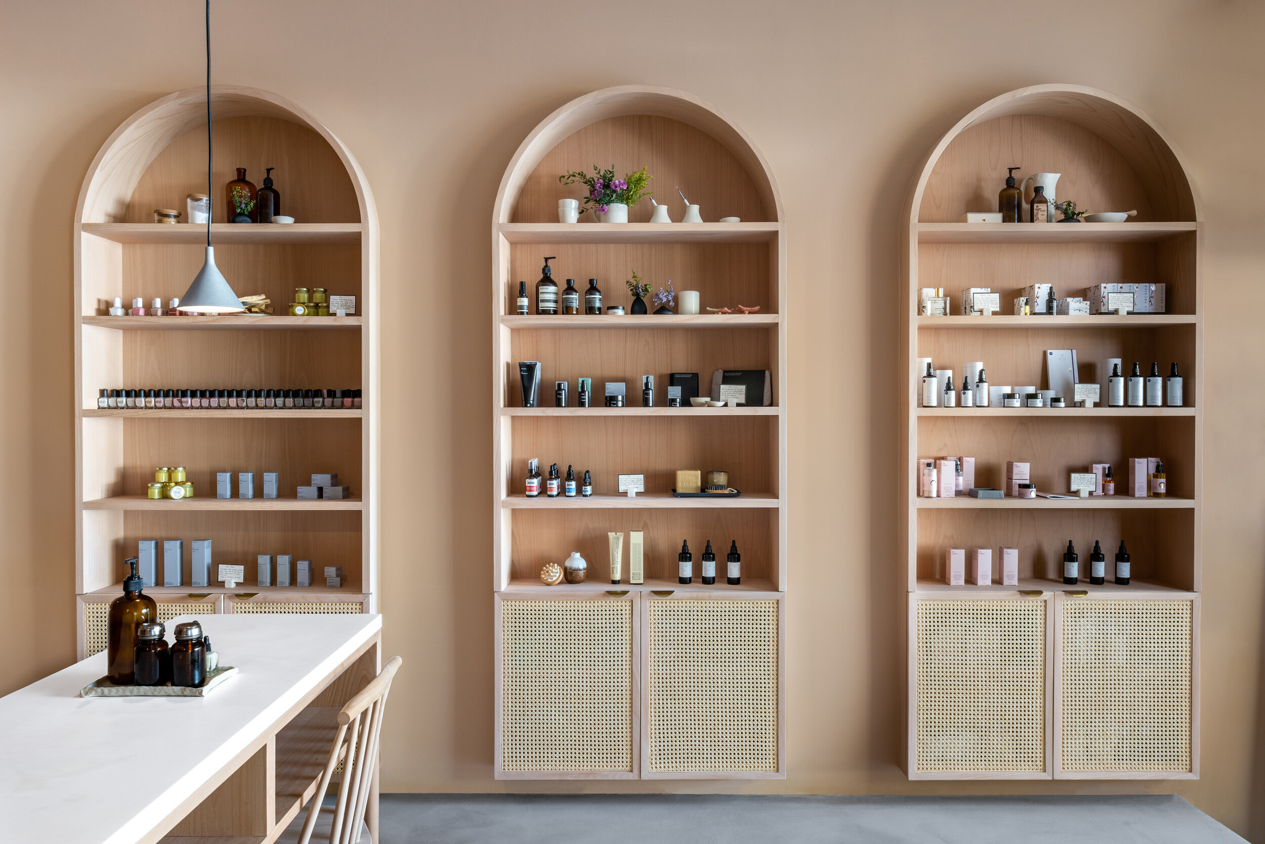 Three built-in arched shelving units with cane panels displaying wellness products and botanicals