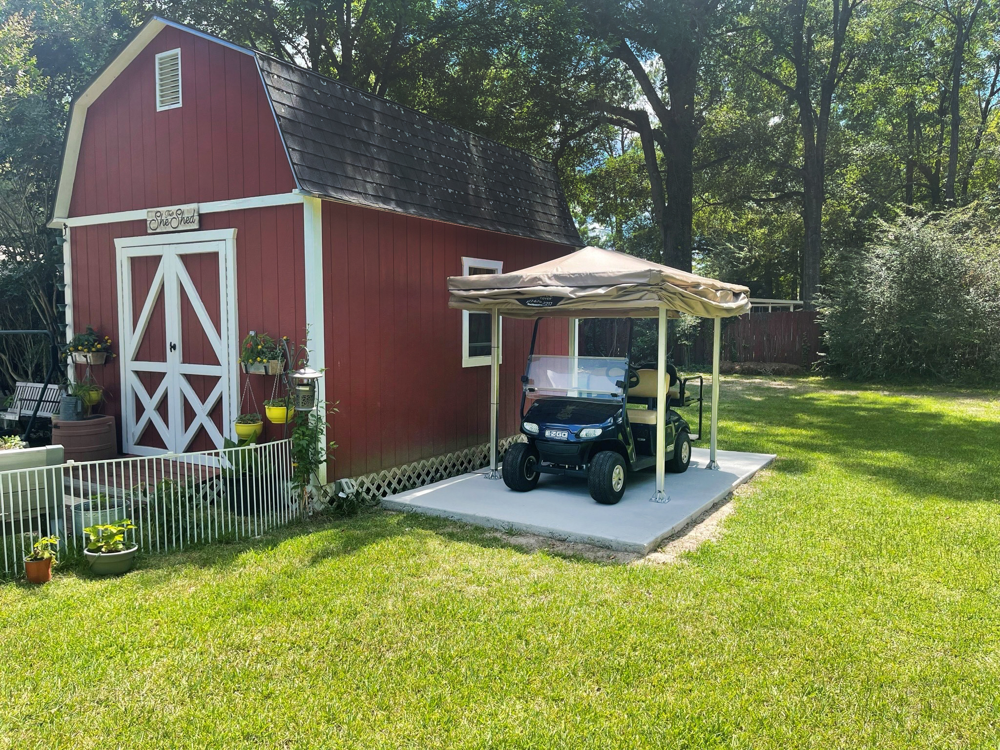 Golf cart under an open tan Touchless Cover canopy next to a red barn shed