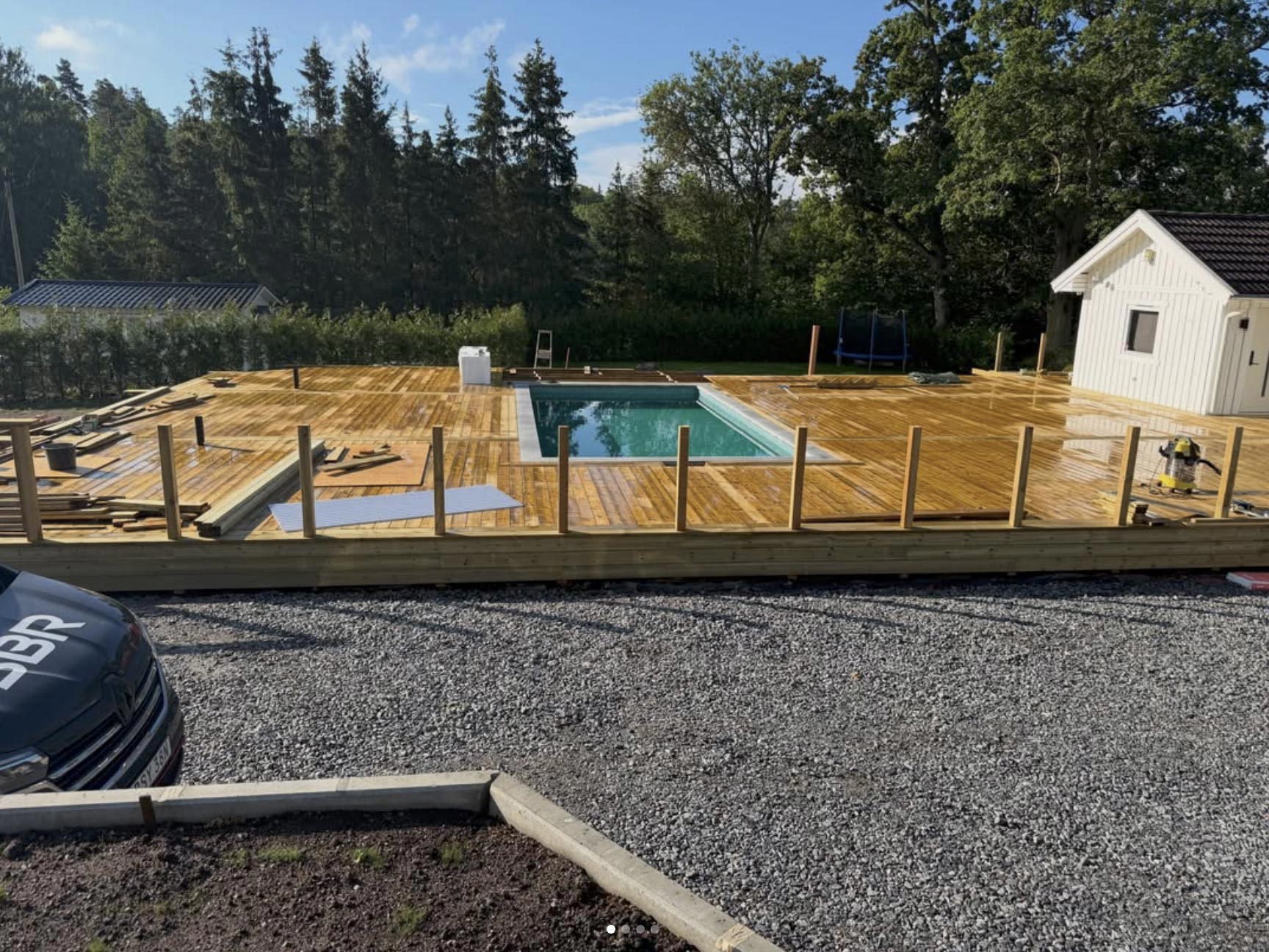 Färdig pool med solig trädäck och grusuppfart