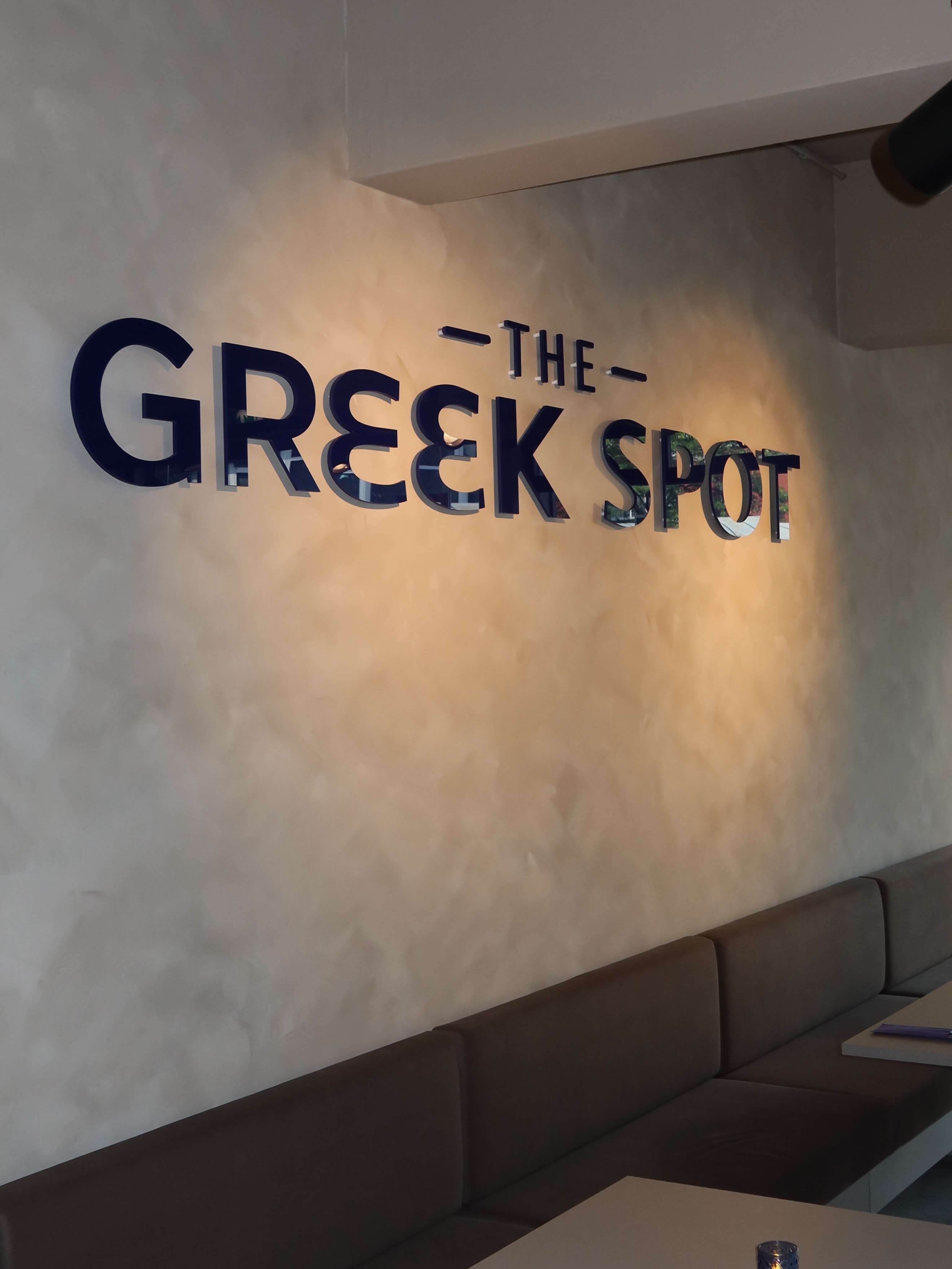 The Greek Spot lettering on a warm plaster wall above a banquette