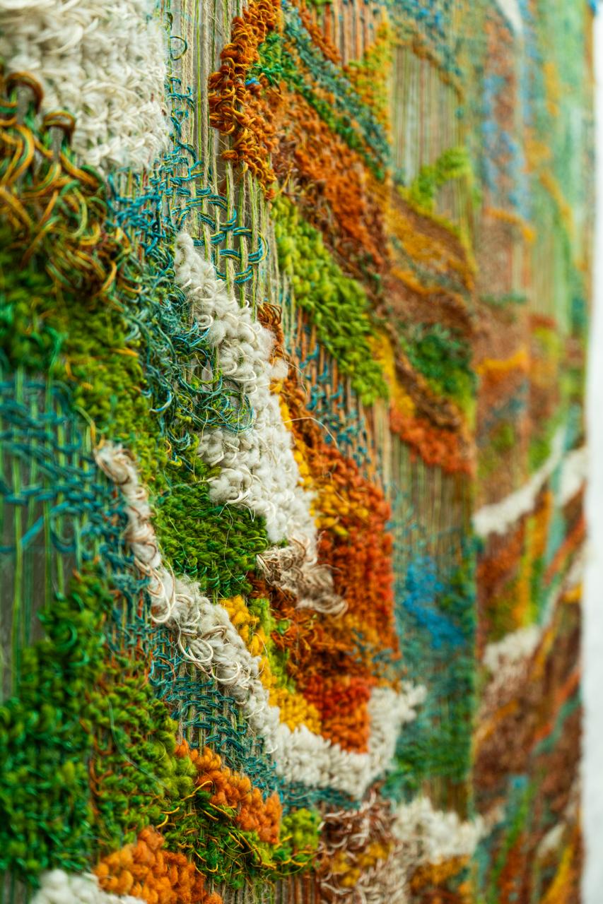 Detalle de tapiz tejido a mano mostrando texturas de hilos en colores verdes, naranjas y blancos