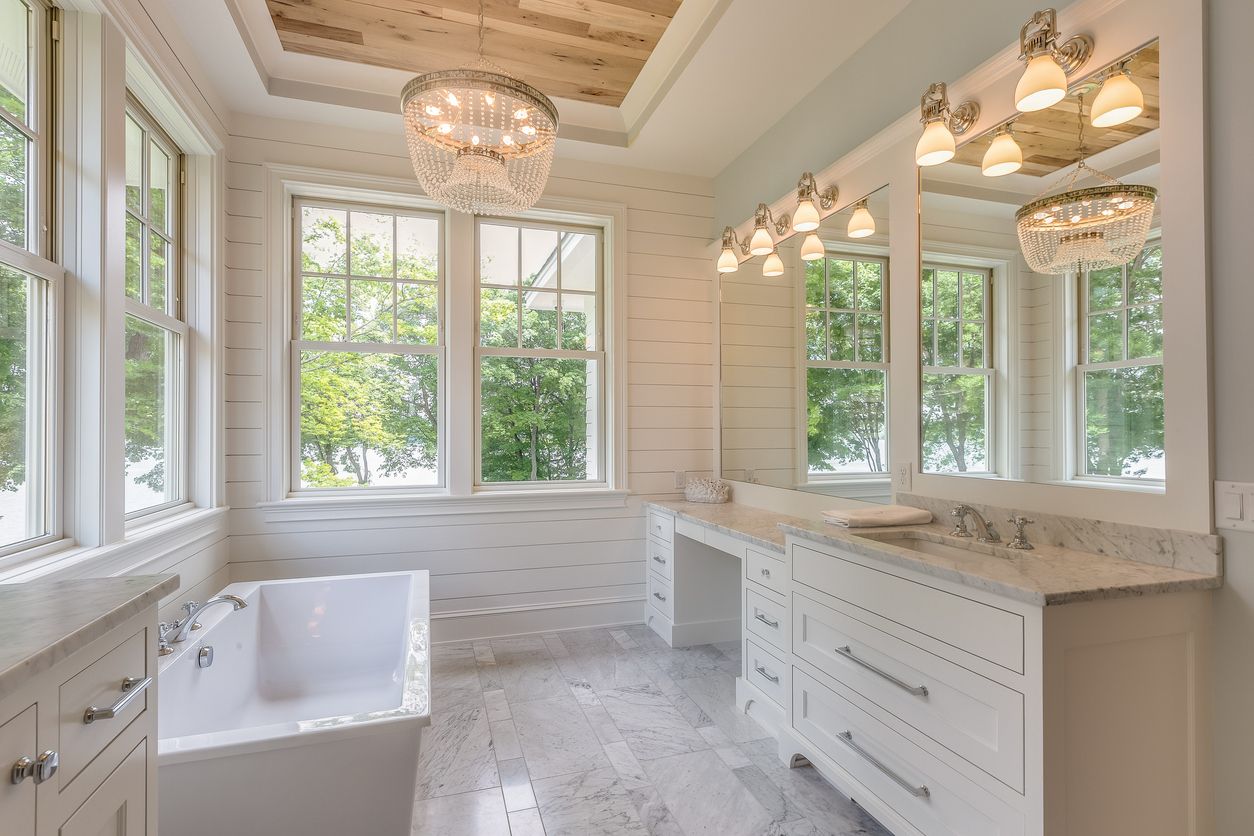 Bright Southern farmhouse bathroom with shiplap walls, a crystal chandelier, marble counters, and a freestanding tub by large windows