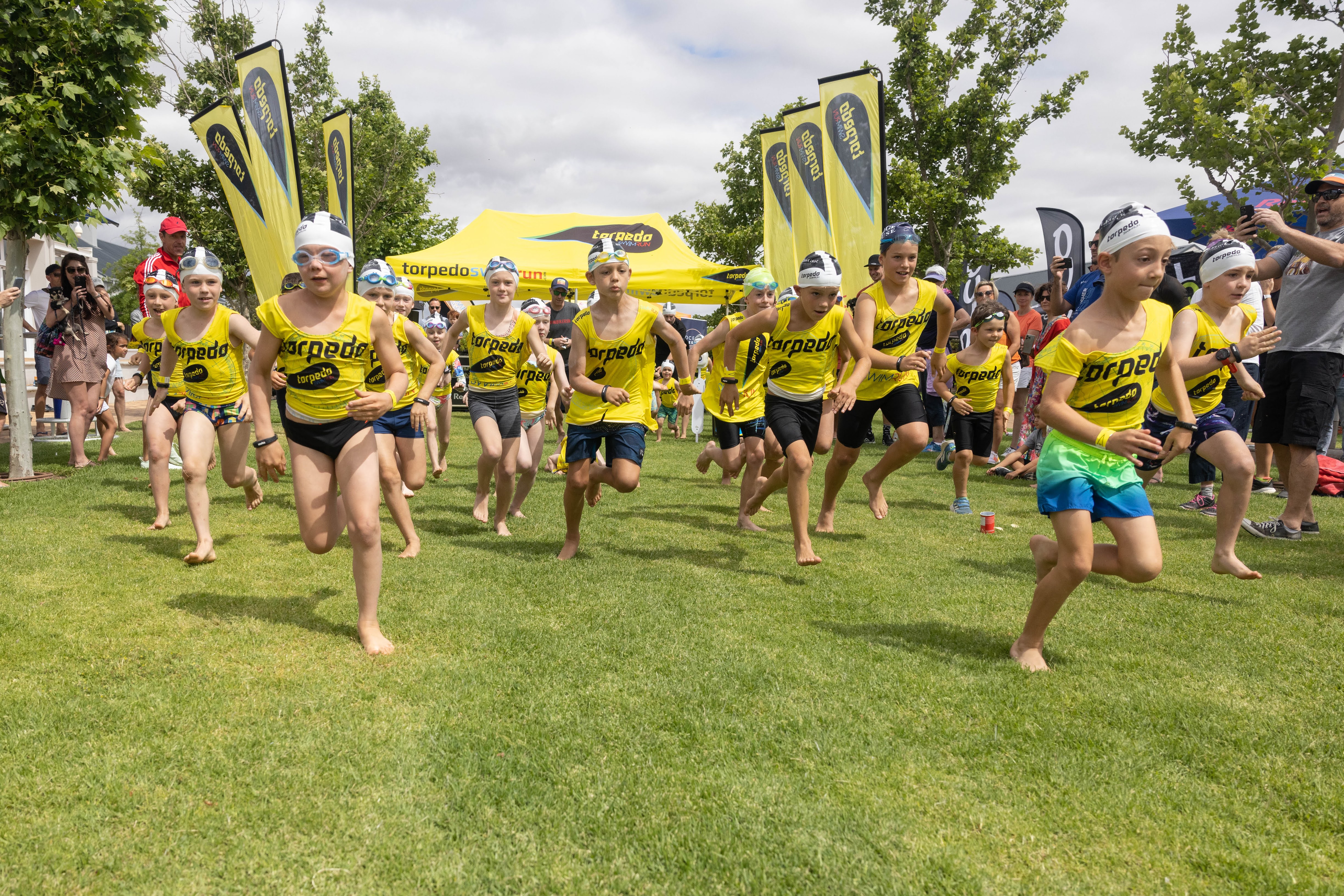 Large group of barefoot kids in yellow vests running on grass