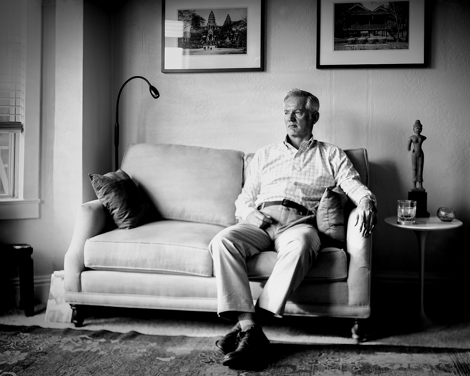 Man seated on sofa in living room with framed photographs of Angkor Wat and house on wall behind him