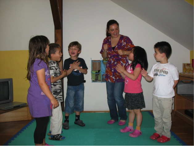 Pädagogin leitet eine Gruppe von fünf Kindern in einem Bewegungsspiel im Gruppenraum