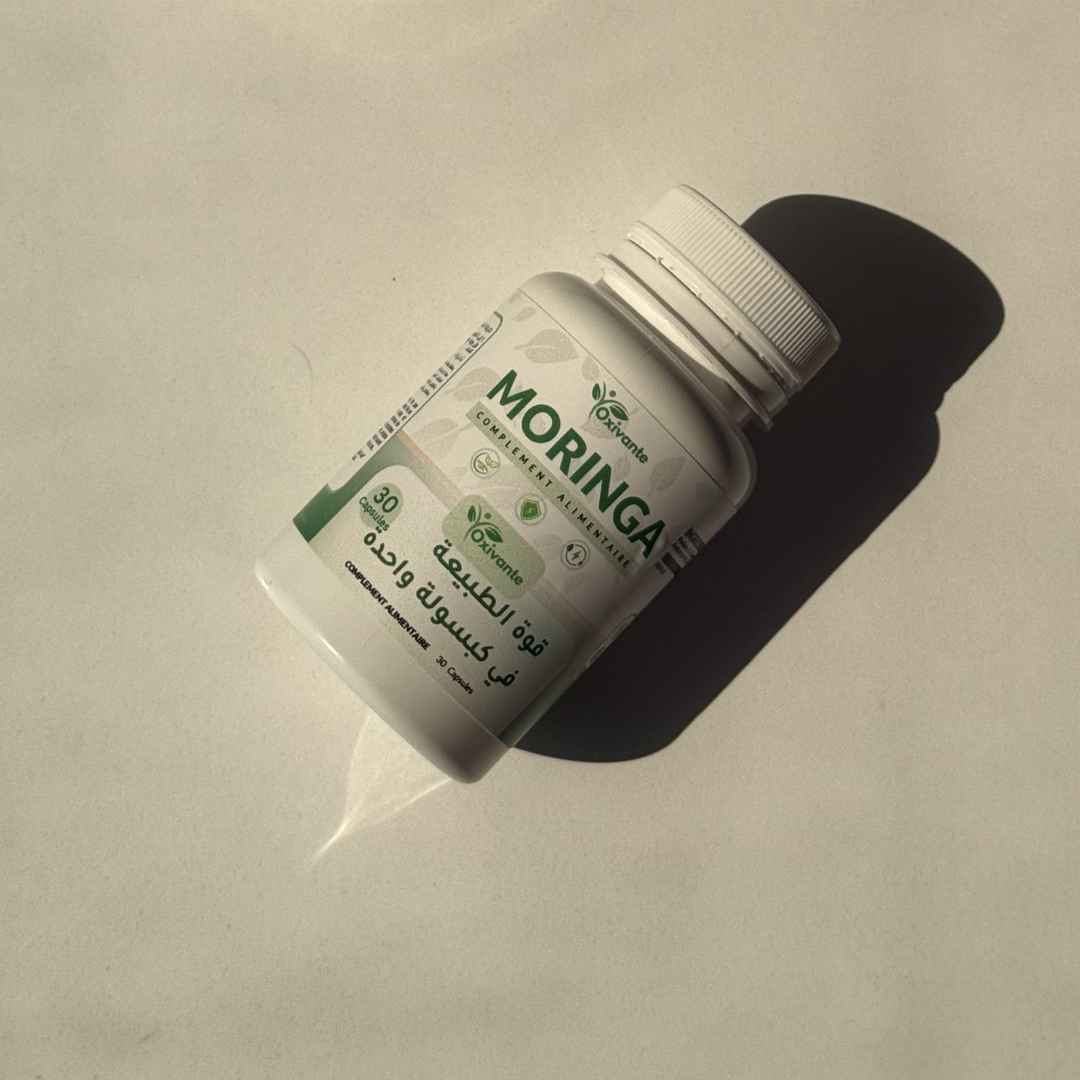 Oxivante Moringa — لقطة علوية للعلبة على خلفية بيج دافئة مع ظل دراماتيكي