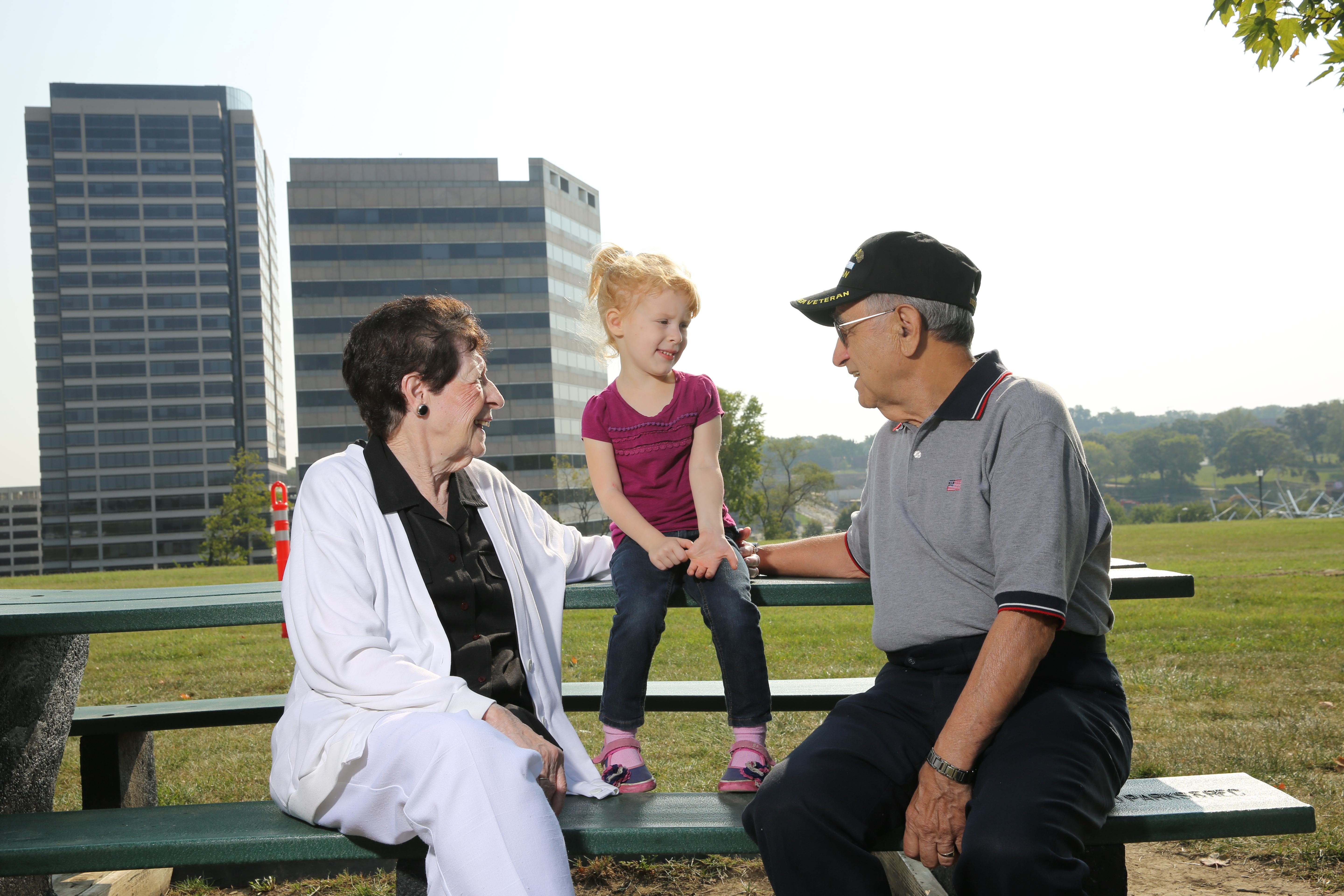 Veteran grandfather with wife and young granddaughter sharing a moment on a park bench