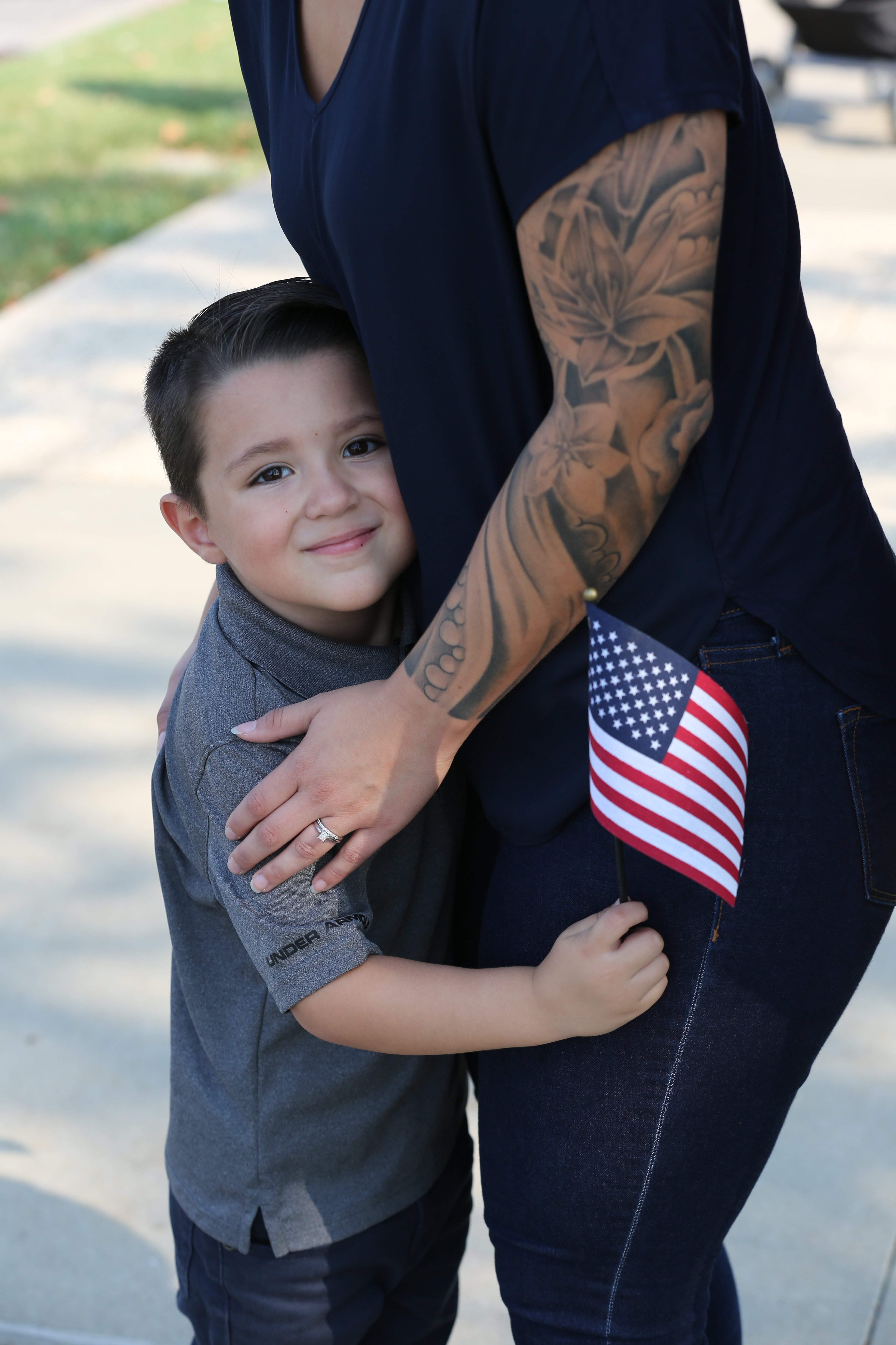 Young boy holding American flag while embracing his mother at a community event