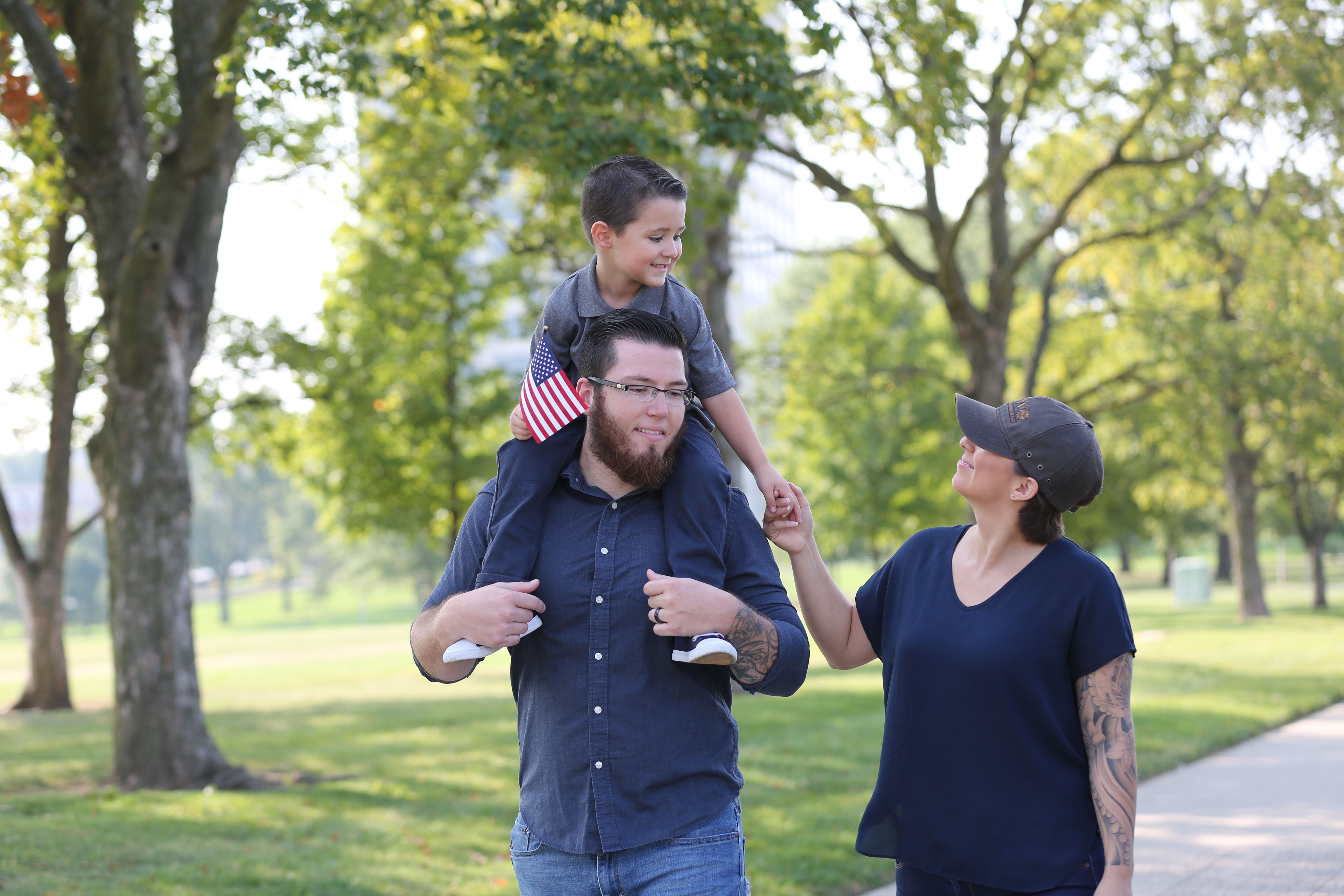 Veteran family walking in a park, child on father's shoulders holding American flag