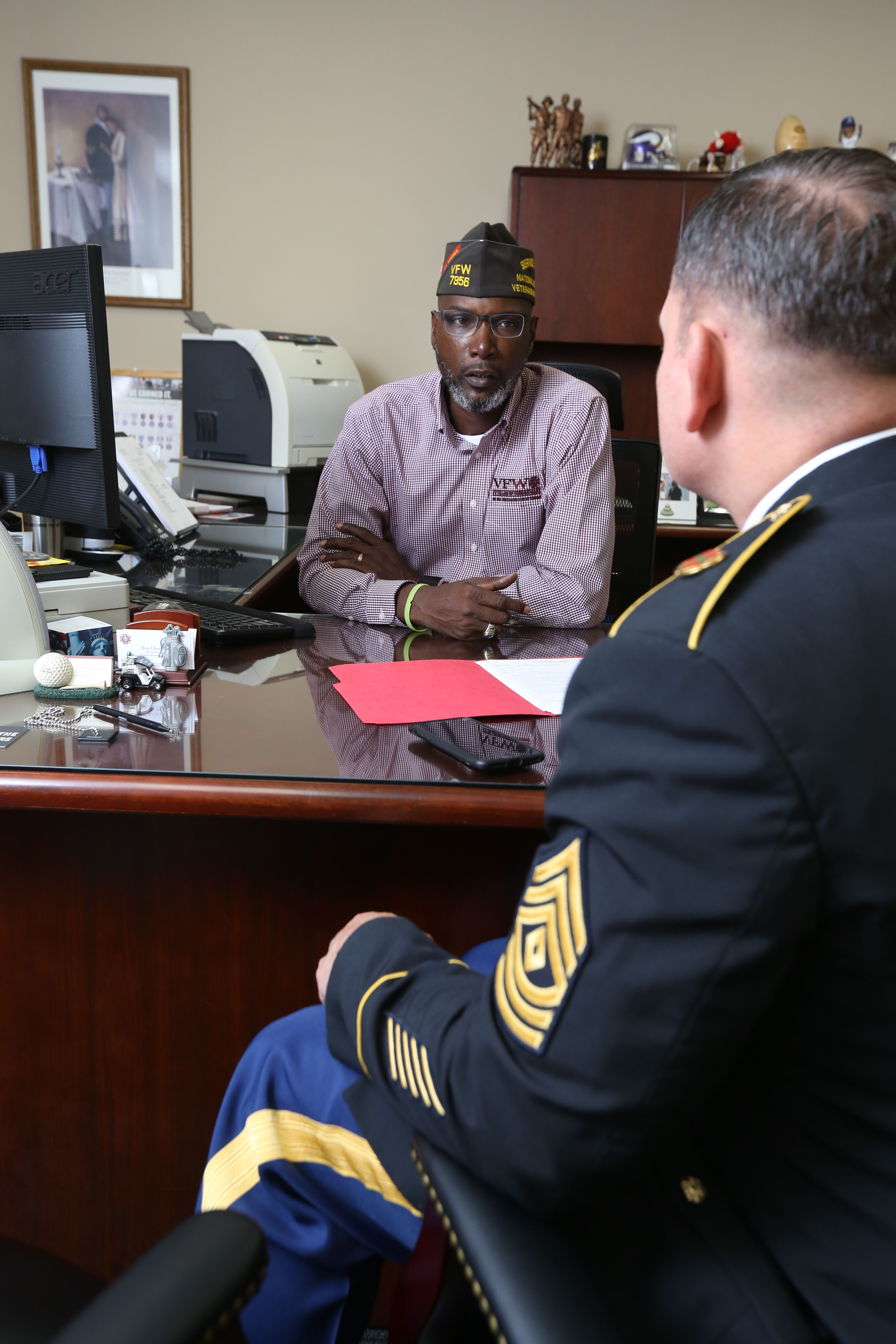 VFW service officer in garrison cap assisting Army sergeant with benefits claim at desk