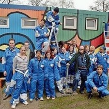 Großes Gruppenbild in blauen Overalls vor dem bemalten Container