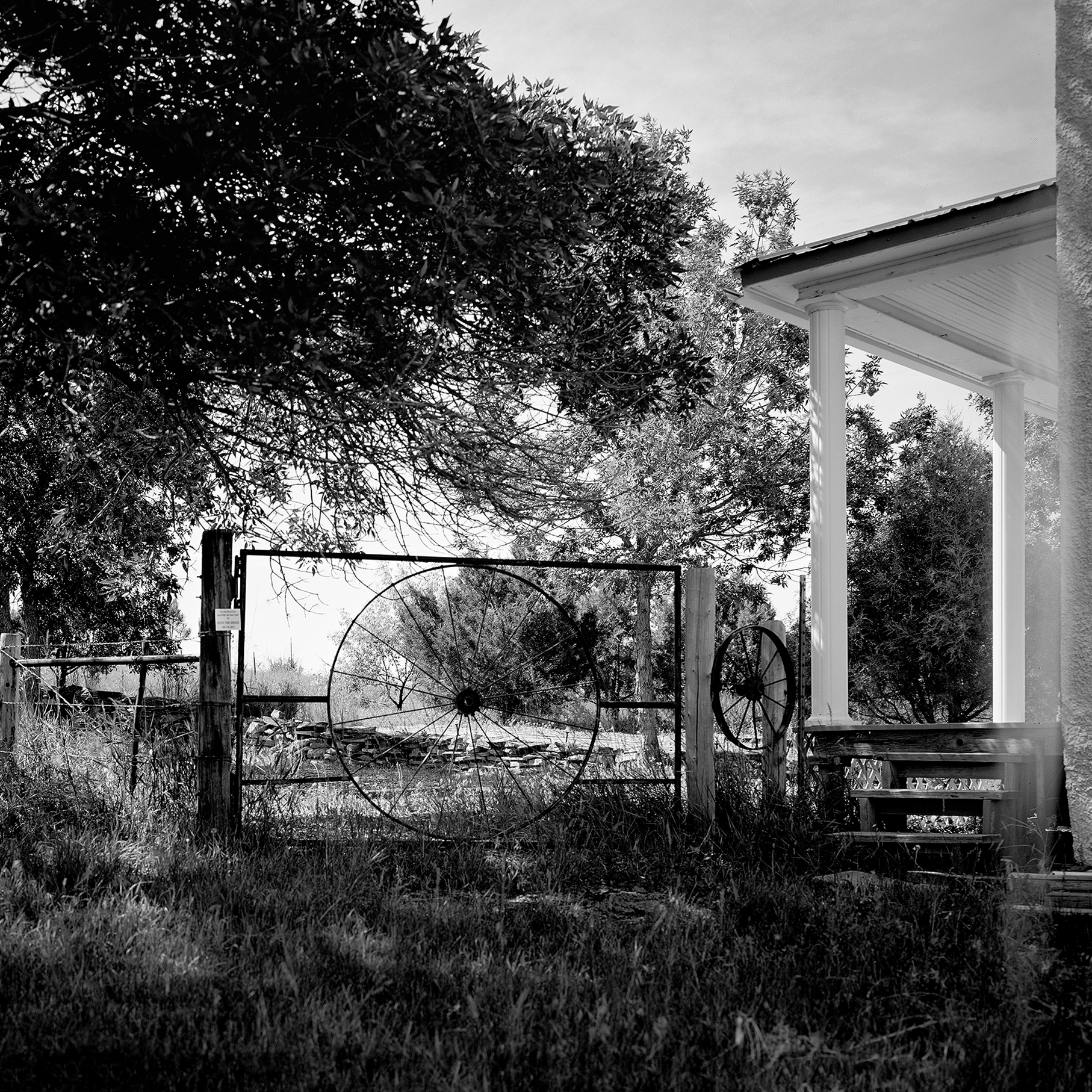 Antique wagon wheels mounted in rustic gate frame beside white columned porch with rural landscape