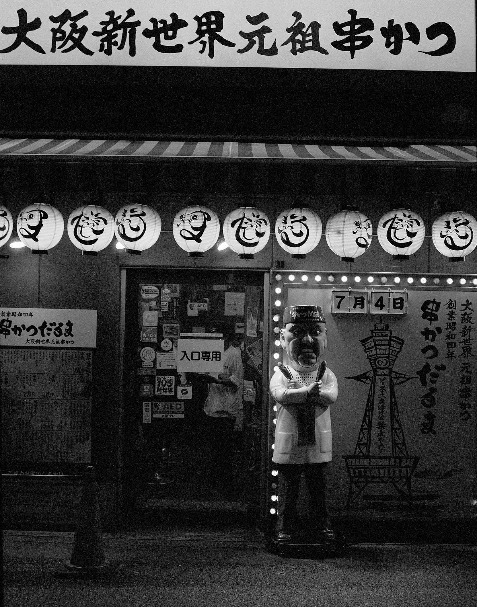 Traditional Japanese street storefront with paper lanterns decorated with kanji characters and kabuki figure statue