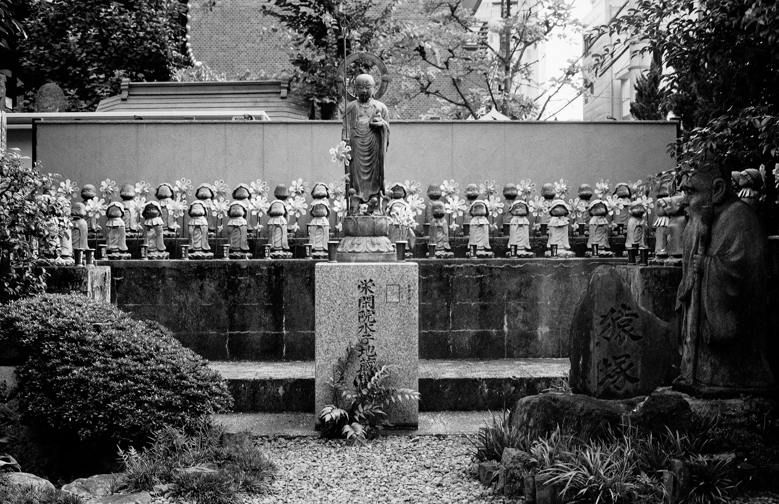 Multiple Jizo statues with halos arranged in rows at temple with carved stone monuments and religious offerings
