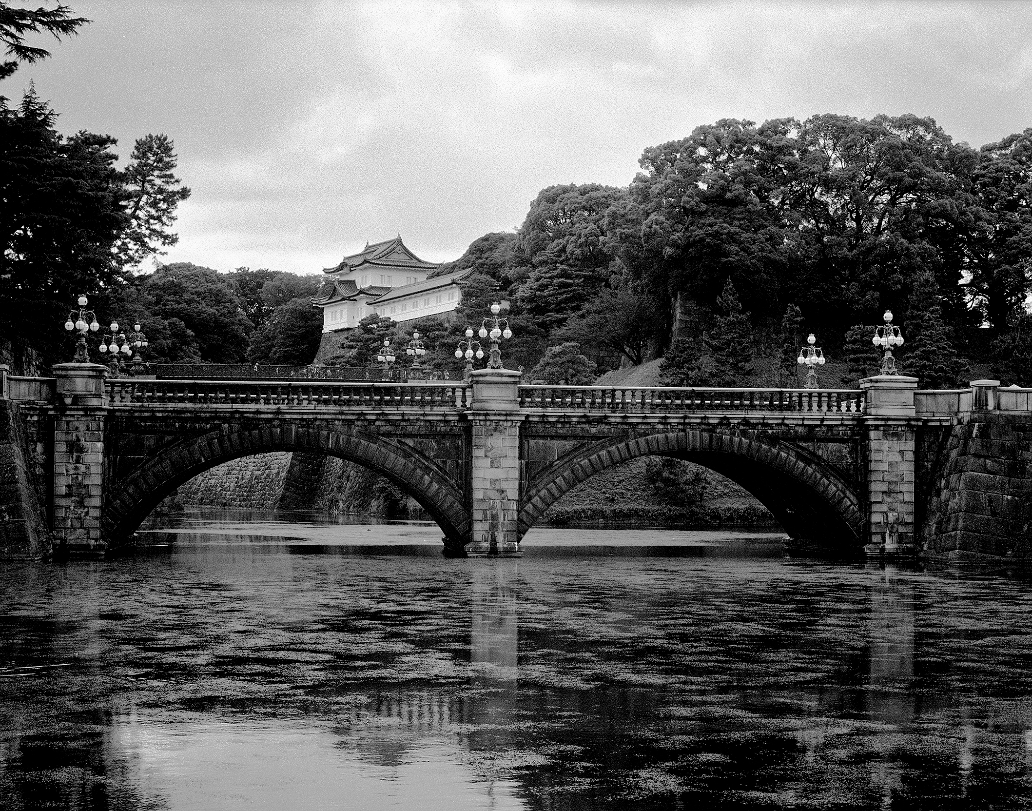 Historic arched stone bridge spanning river with castle pagoda visible through trees and lush forest