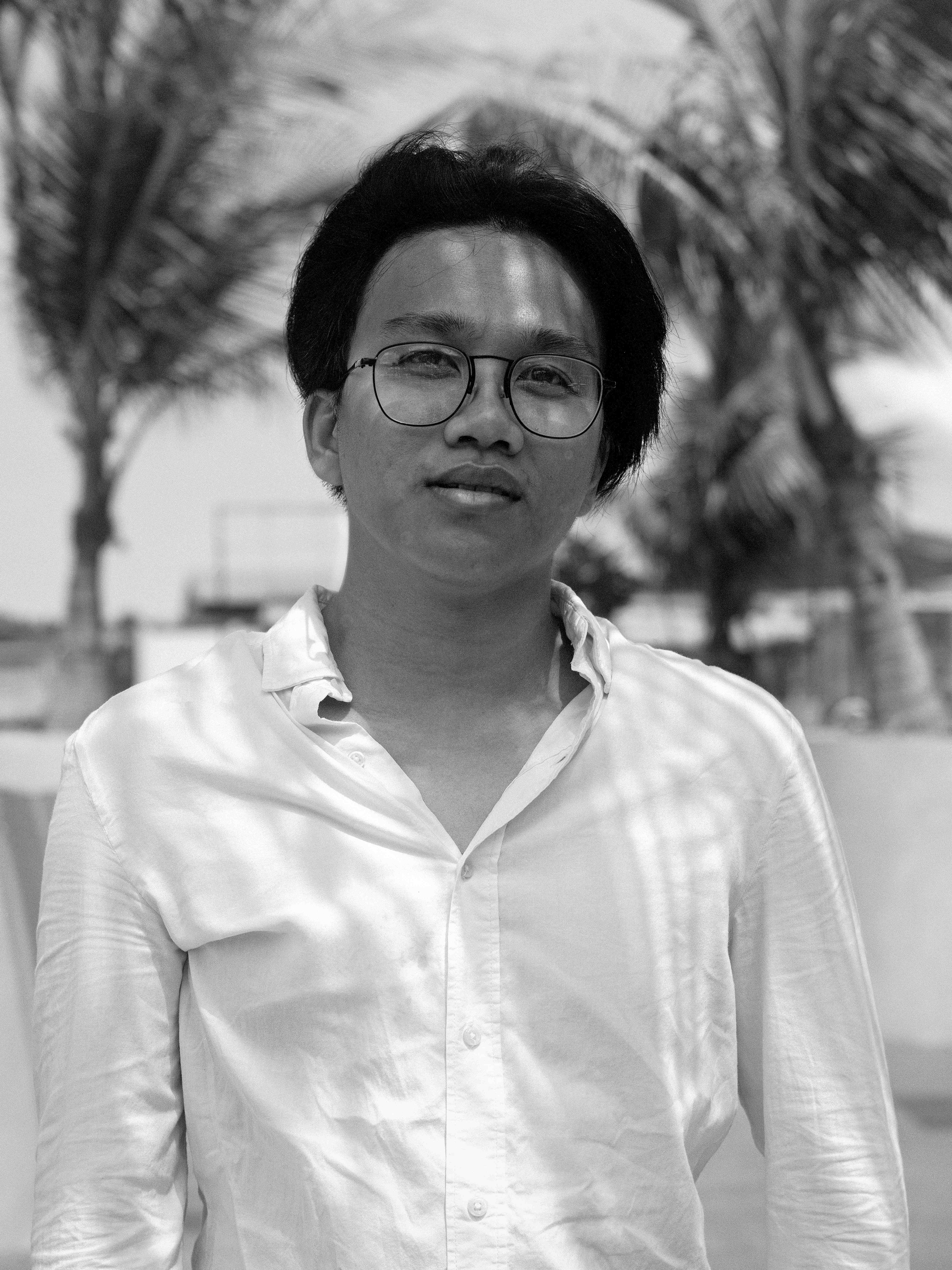 Portrait of young man wearing glasses and white shirt with palm trees in bright tropical background