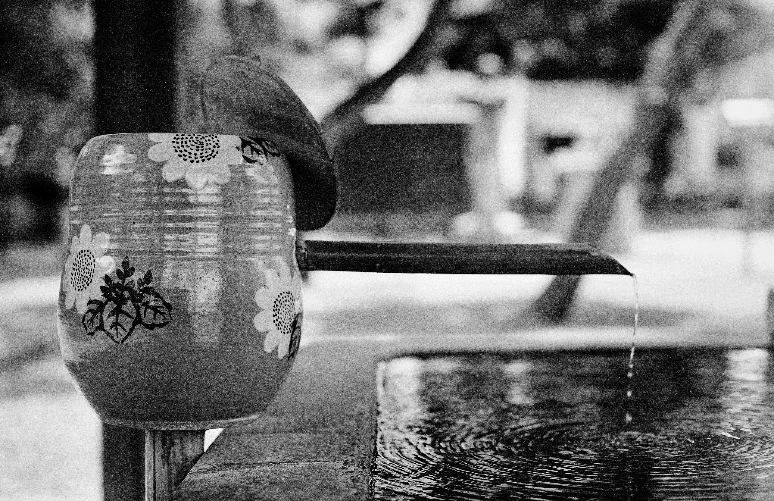 Decorated water basin with floral sunflower pattern and bamboo ladle pouring water in temple courtyard