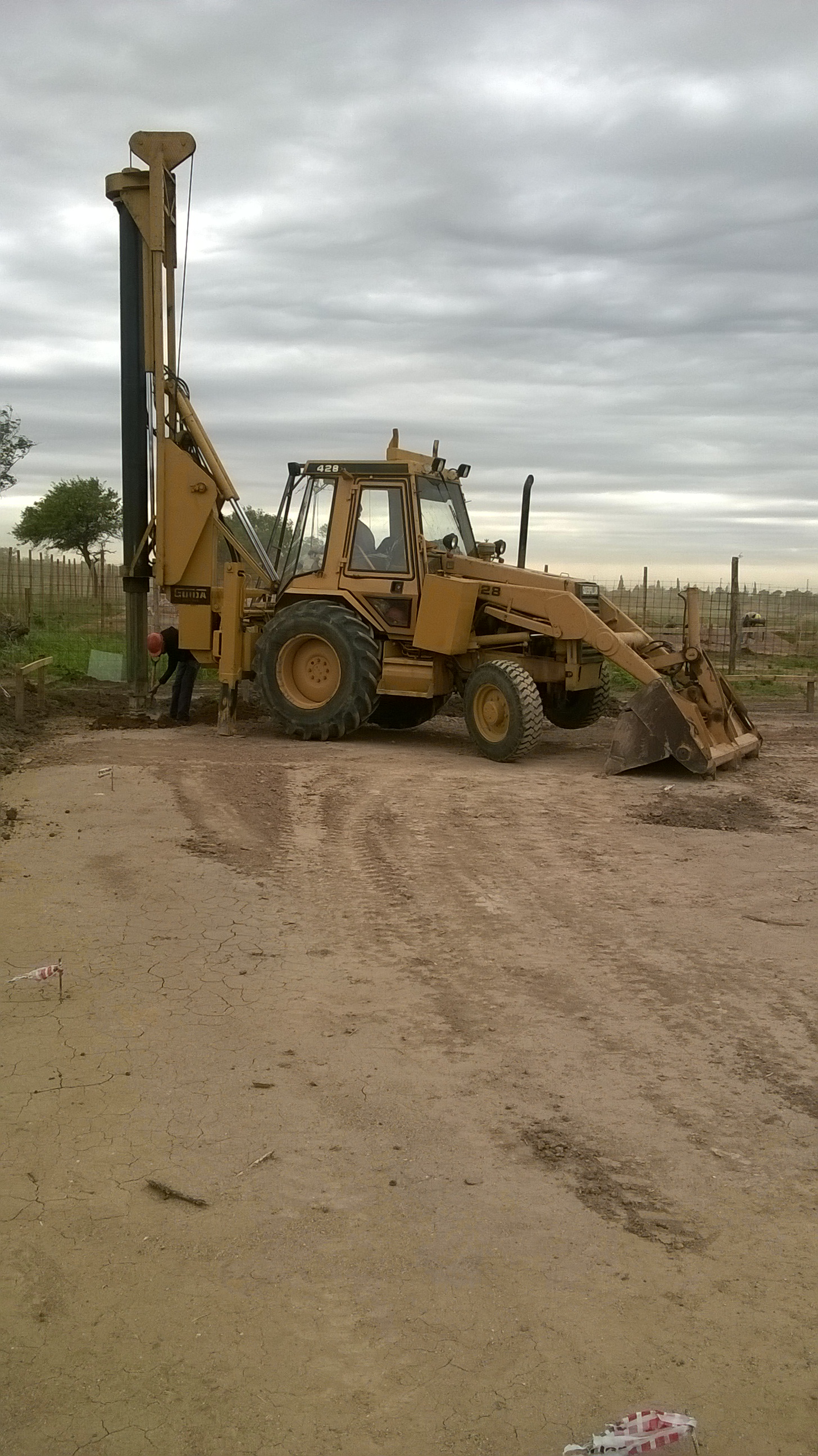 Retroexcavadora con perforadora en terreno rural