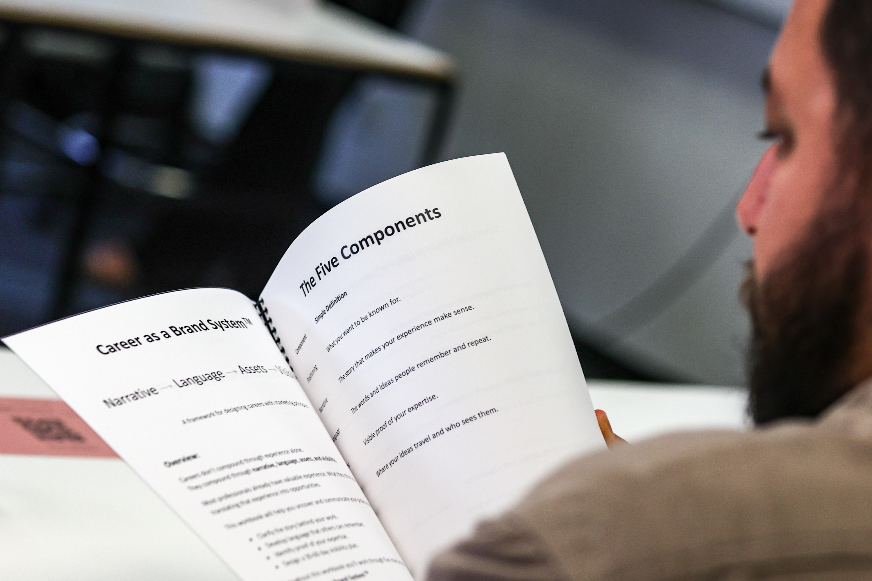 Over-the-shoulder view of an attendee reading the workbook page titled The Five Components