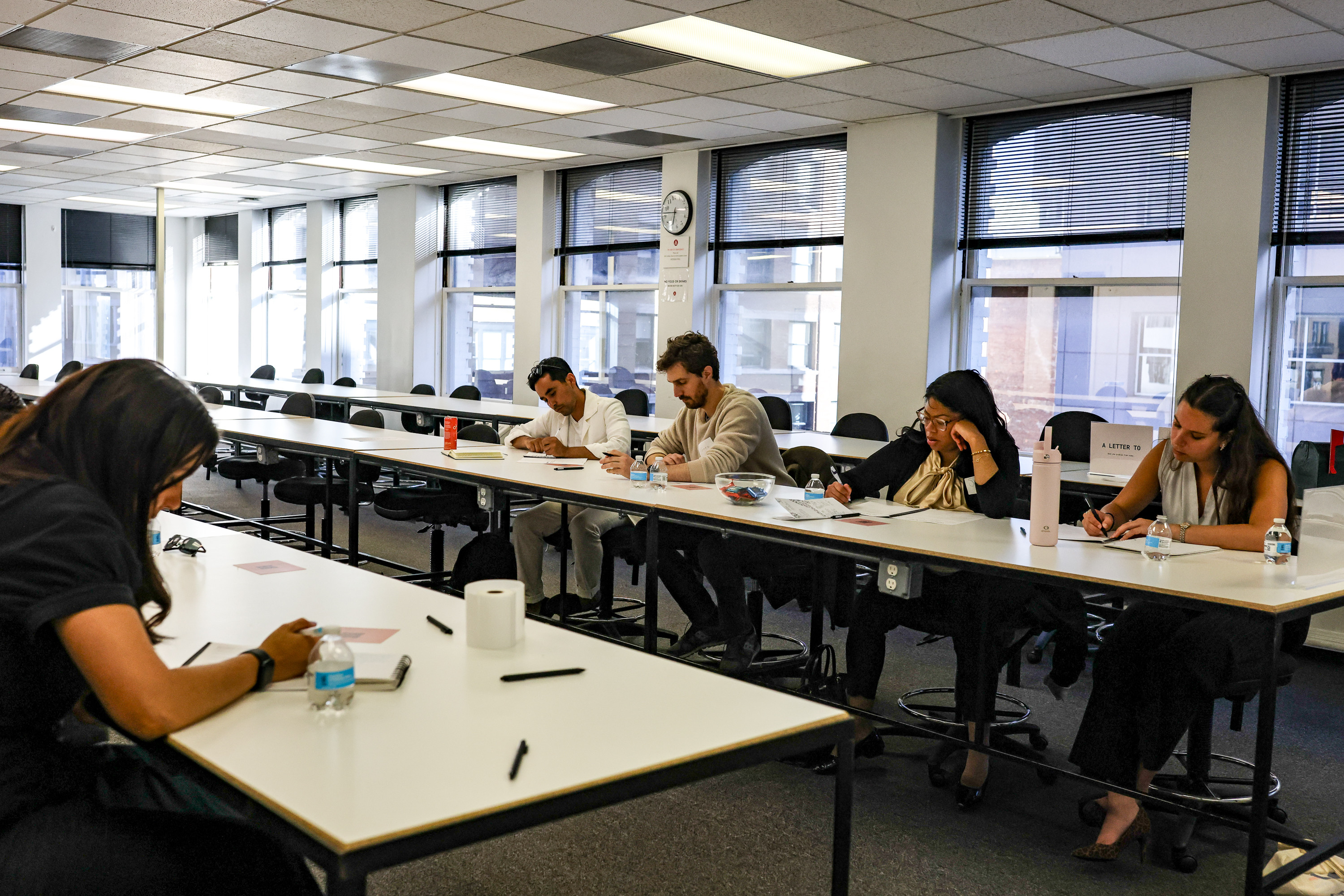 Participants writing quietly at long white tables in the classroom