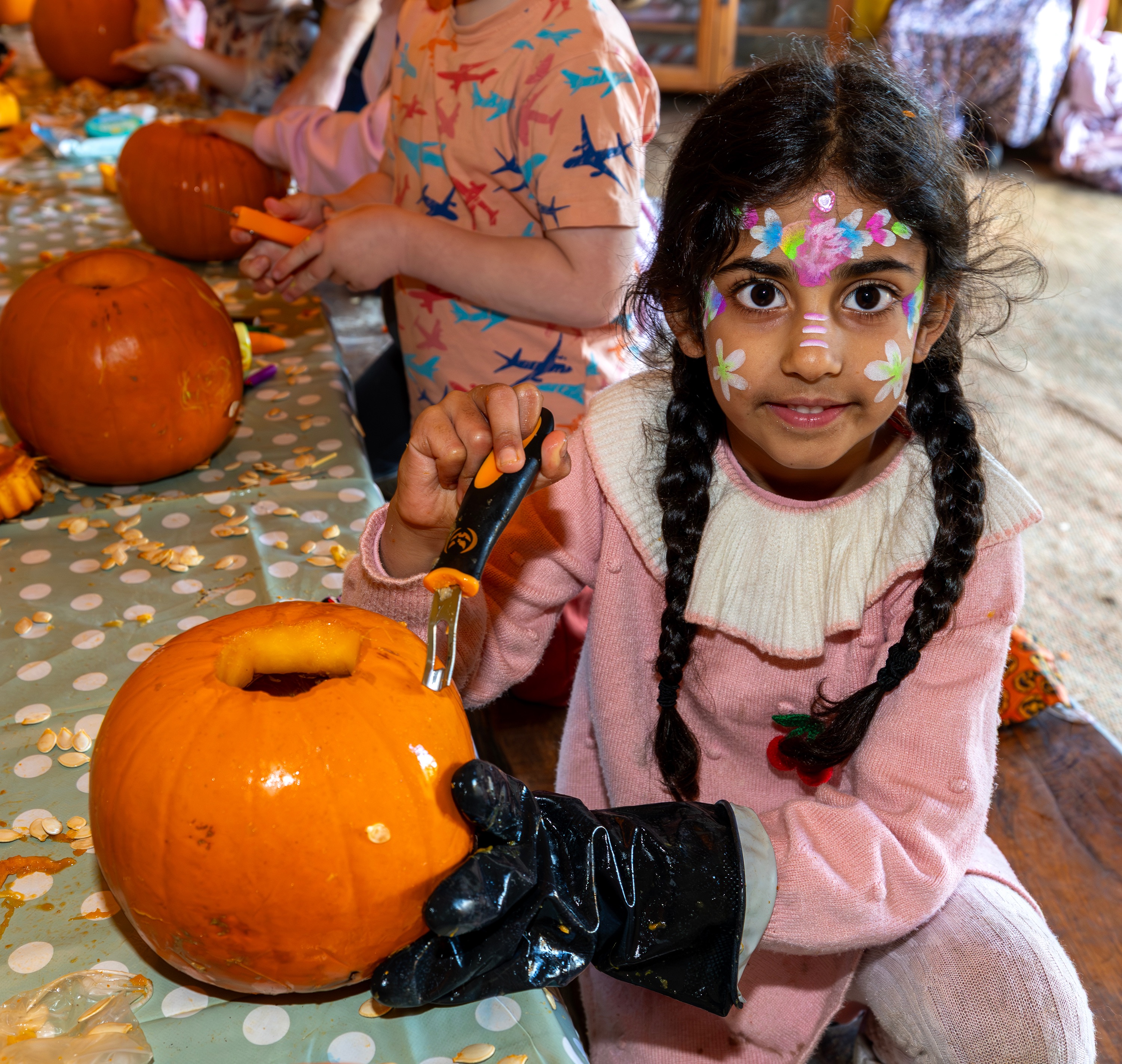 Young girl with face paint carefully carving a pumpkin at a SEND Fest craft activity