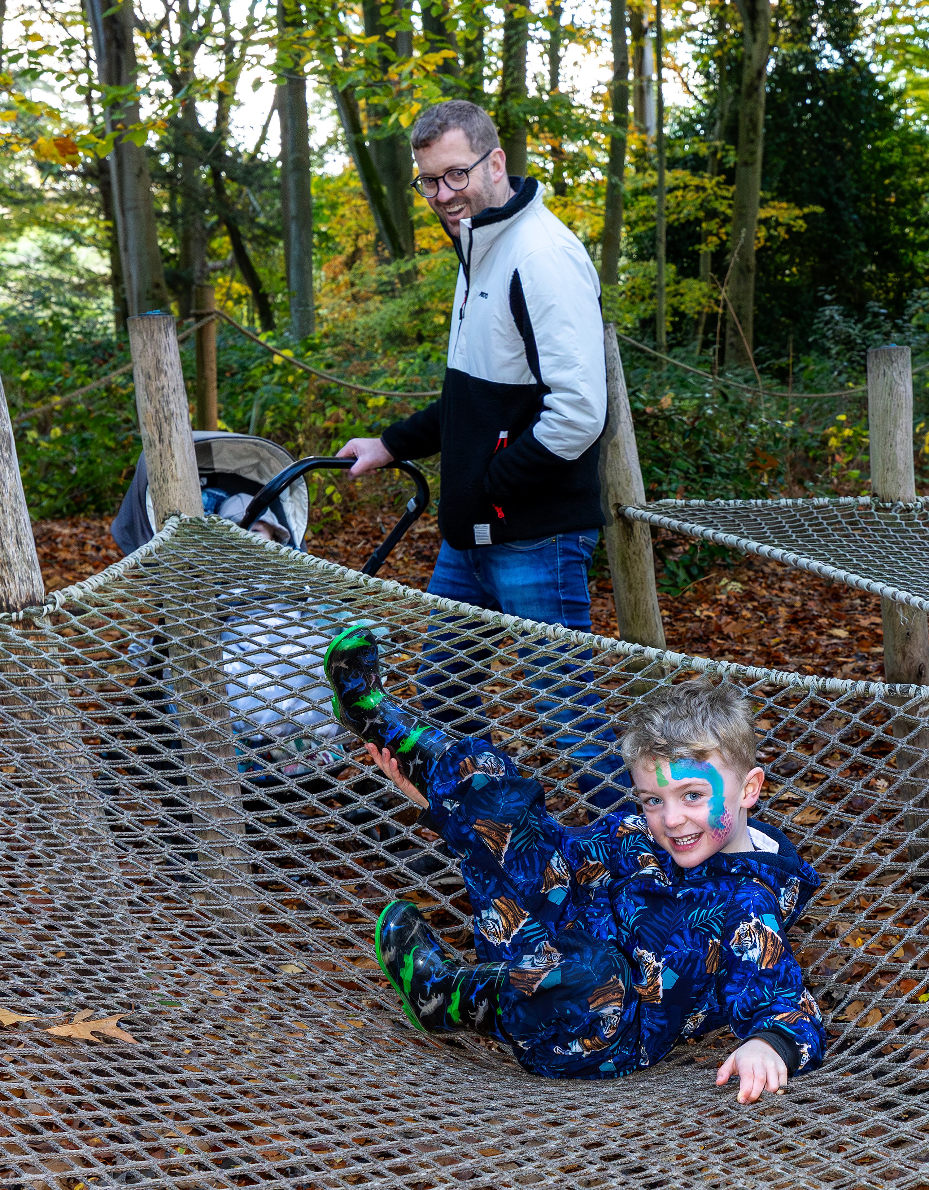Child with face paint playing on a rope net while dad watches with a pushchair at Wyvernwood