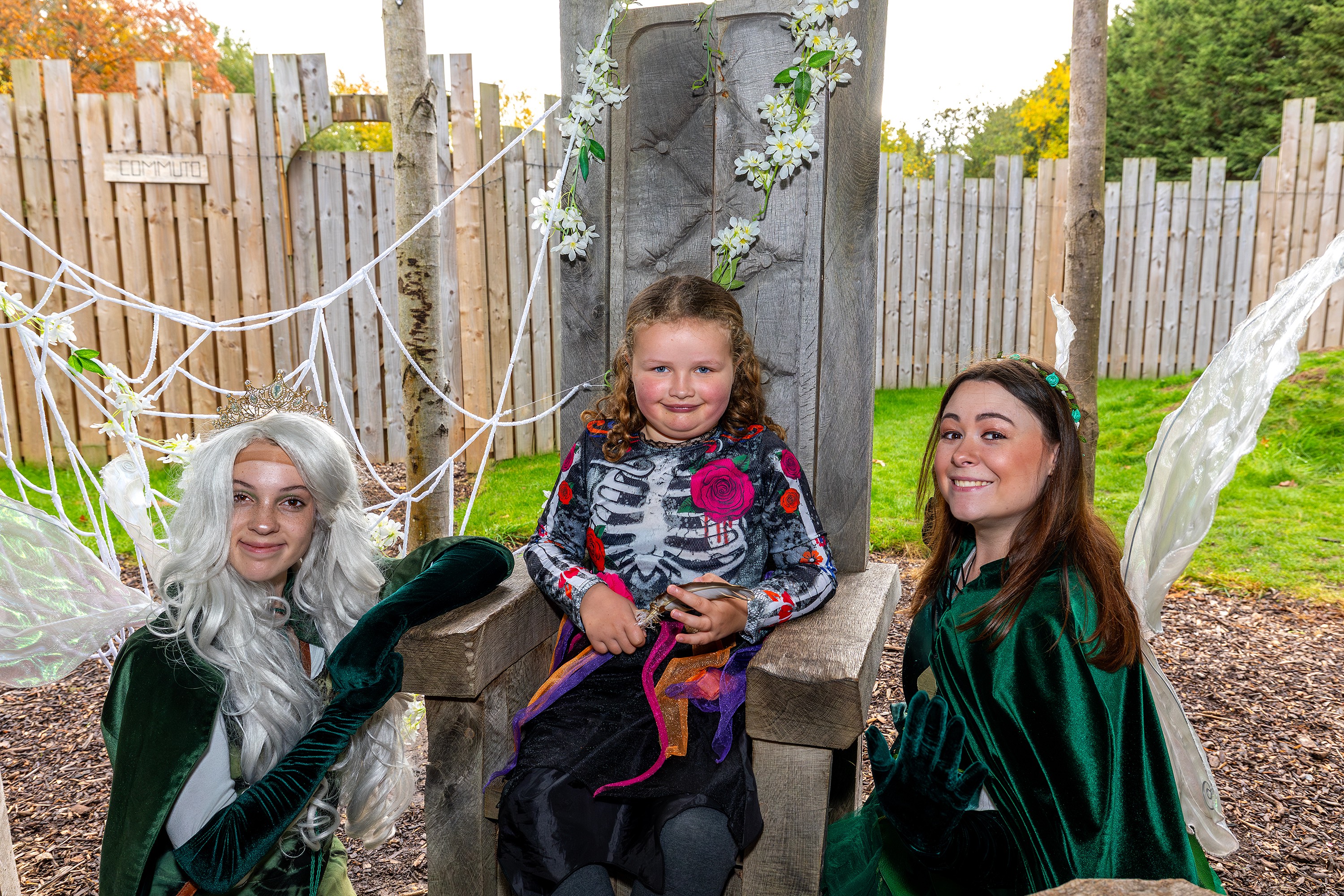 Girl sitting on a woodland throne with two fairy characters at Wyvernwood SEND Fest