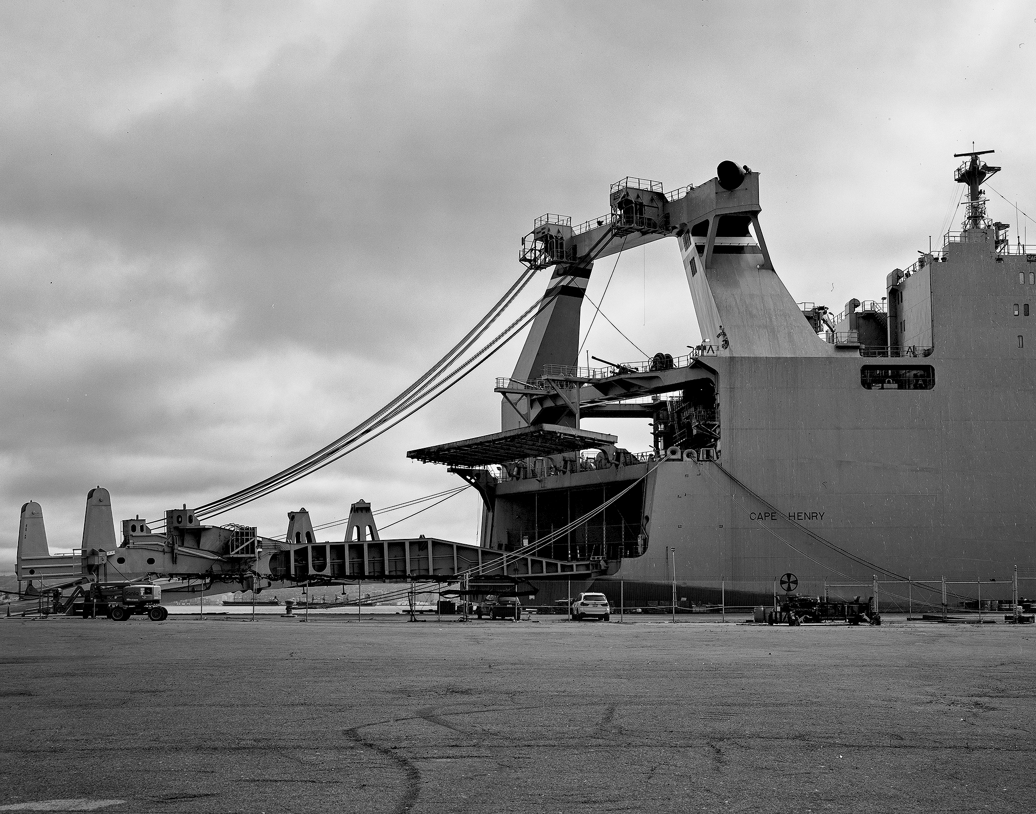 Industrial cargo ship at dock with large loading crane equipment, cables, and port infrastructure against overcast sky