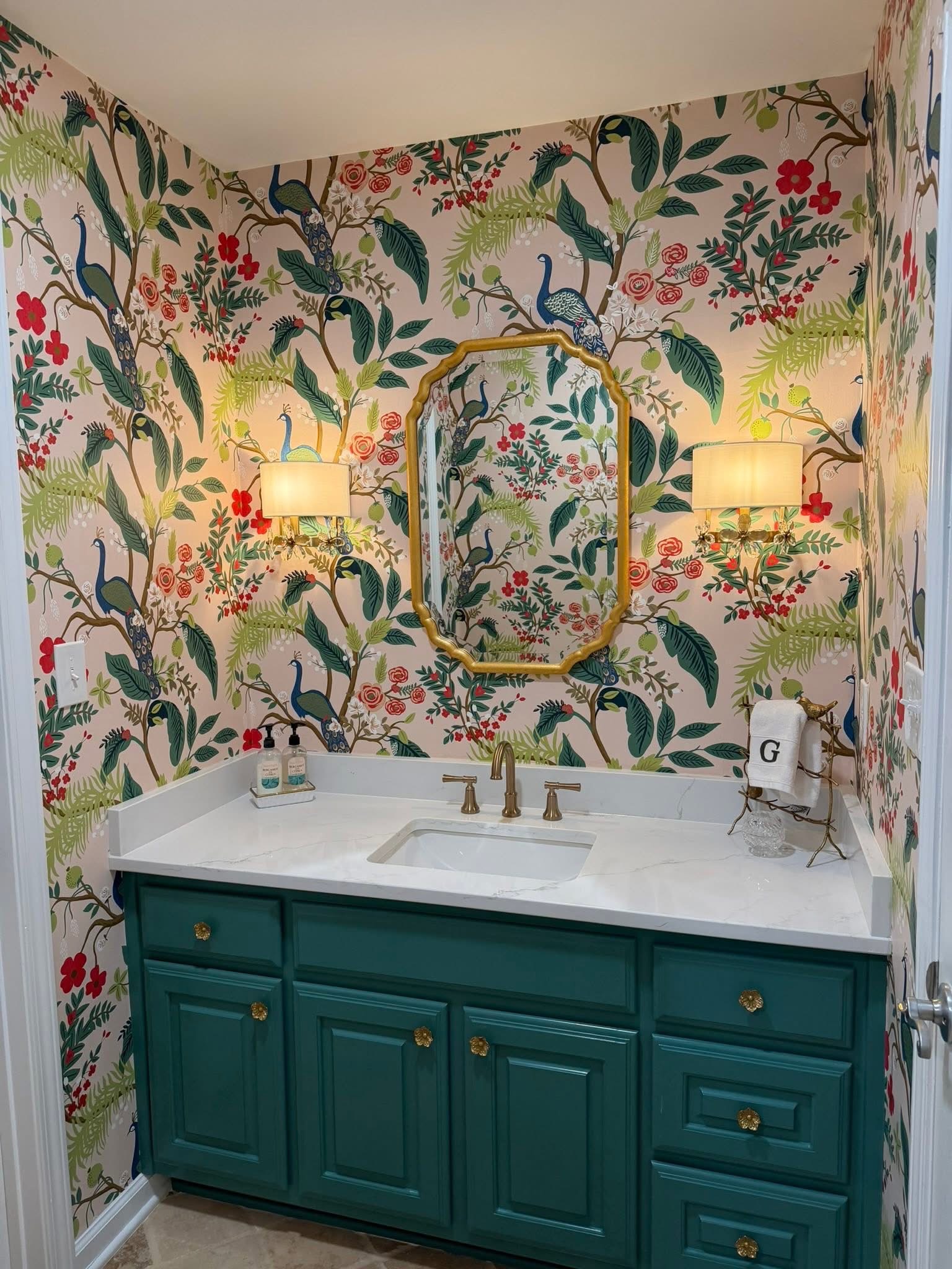 Powder room with vivid peacock-and-floral chinoiserie wallpaper, a gold mirror, and a teal vanity