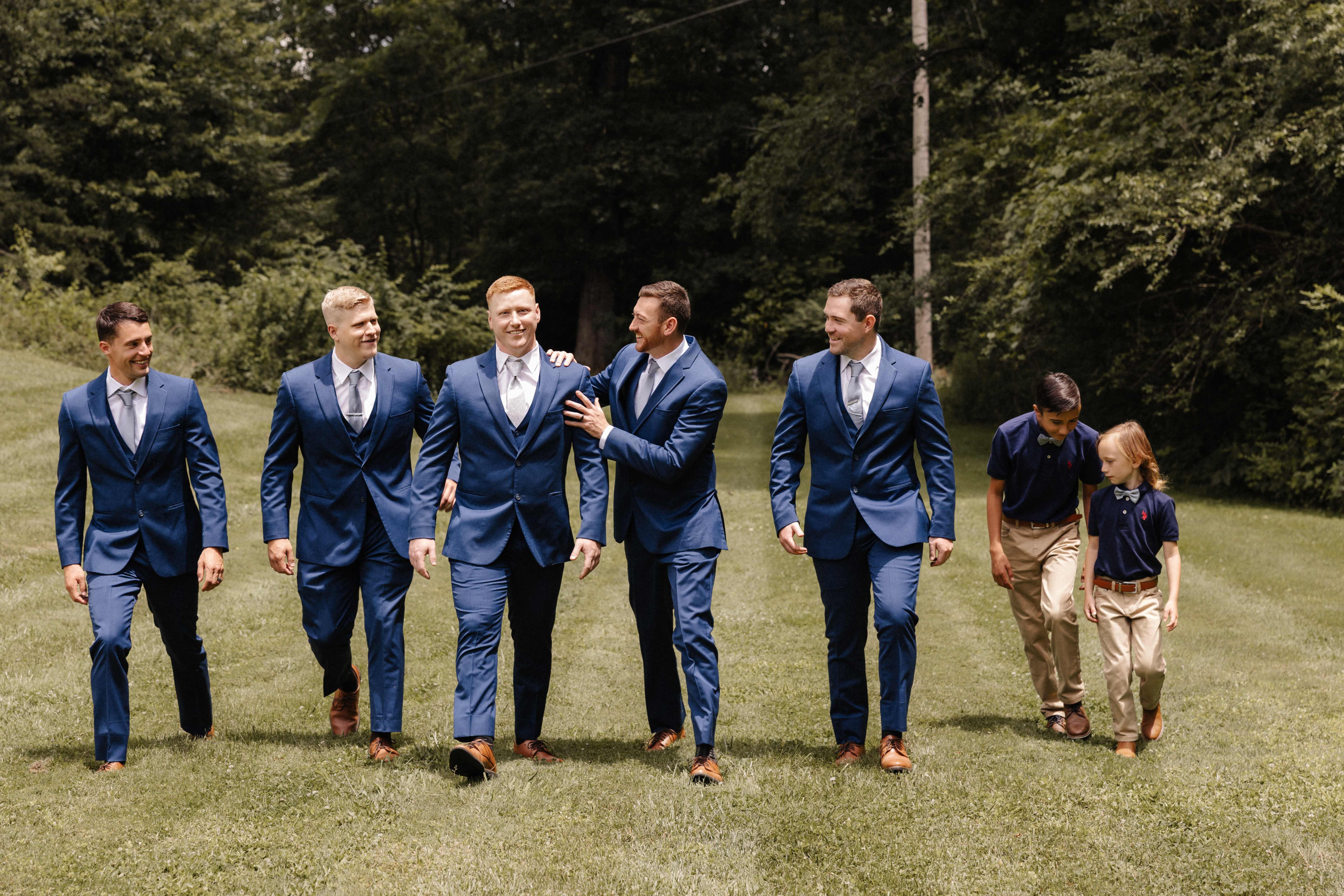 Groomsmen walking in navy suits with young ring bearers