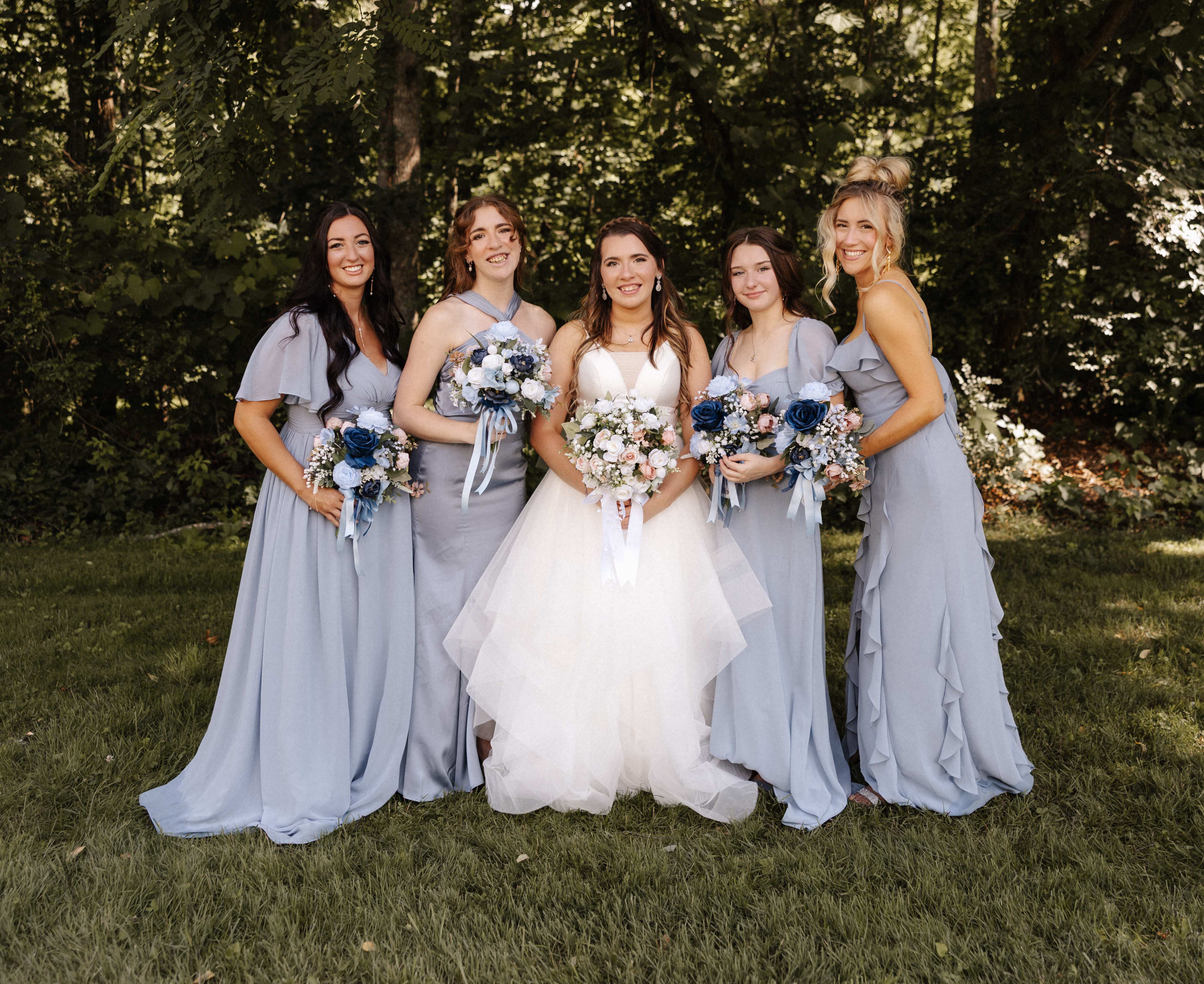 Bride with bridesmaids in dusty blue dresses holding bouquets