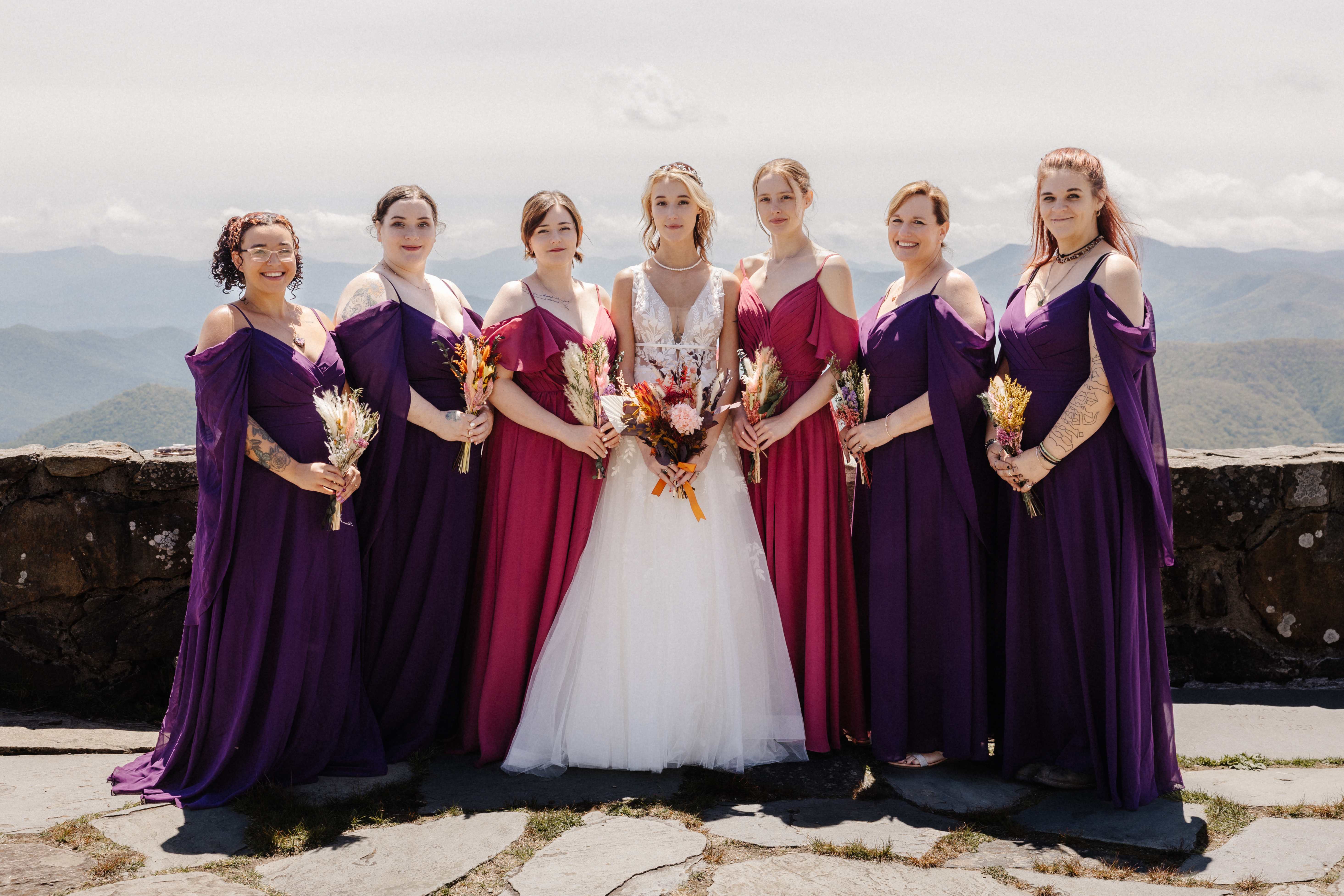 Bride with bridesmaids in purple and magenta dresses with dried flower bouquets