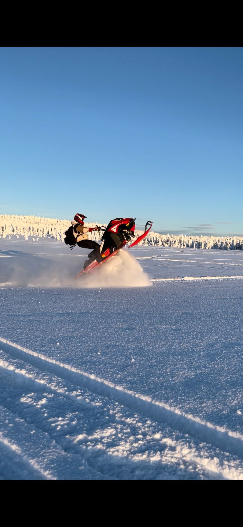 Red snowmobile catching air in spectacular jump over snowy terrain